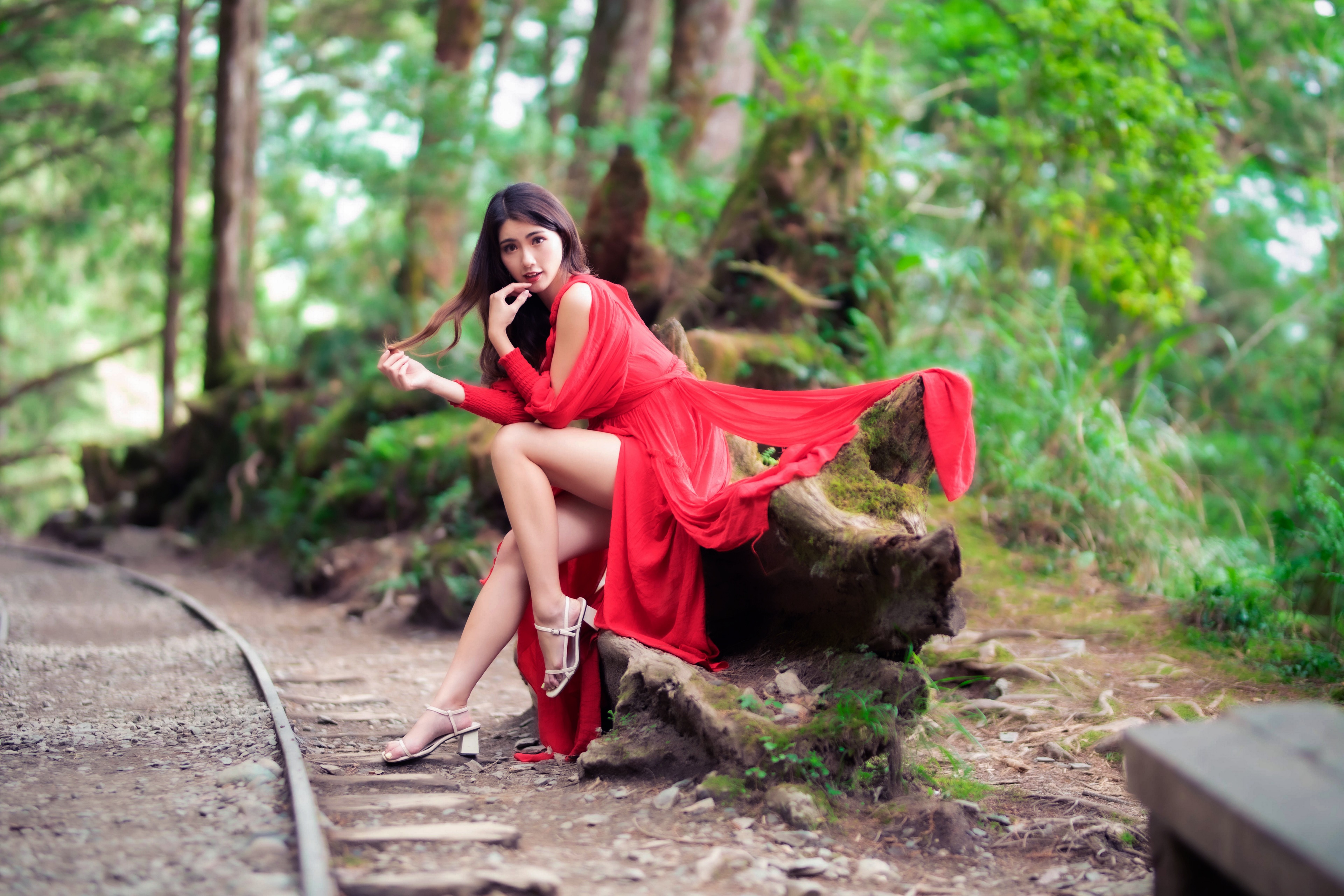Asian woman in red dress sitting by railroad tracks HD Wallpaper