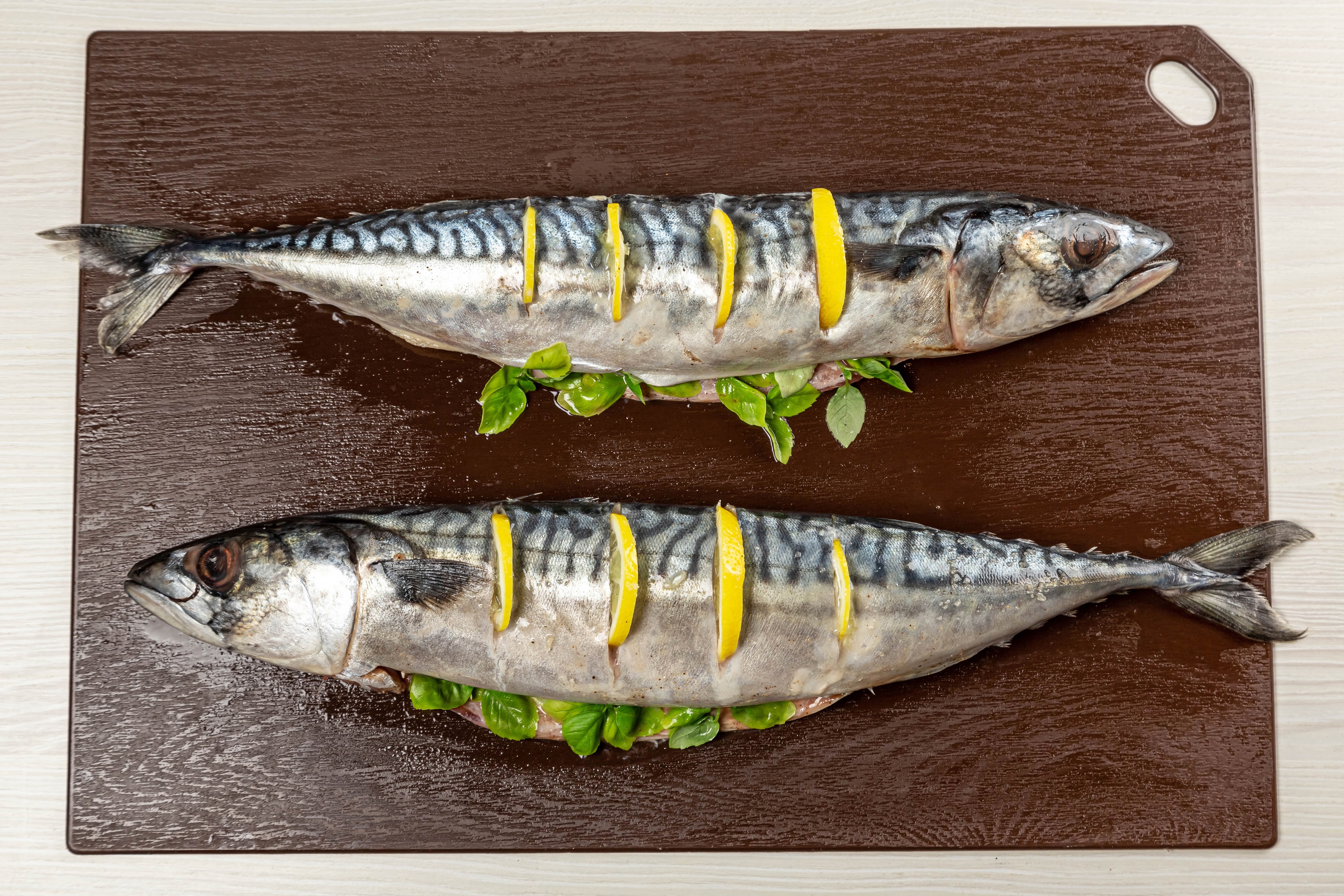 Two Mackerel Fish with Lemon Slices and Herbs on Cutting Board HD Wallpaper