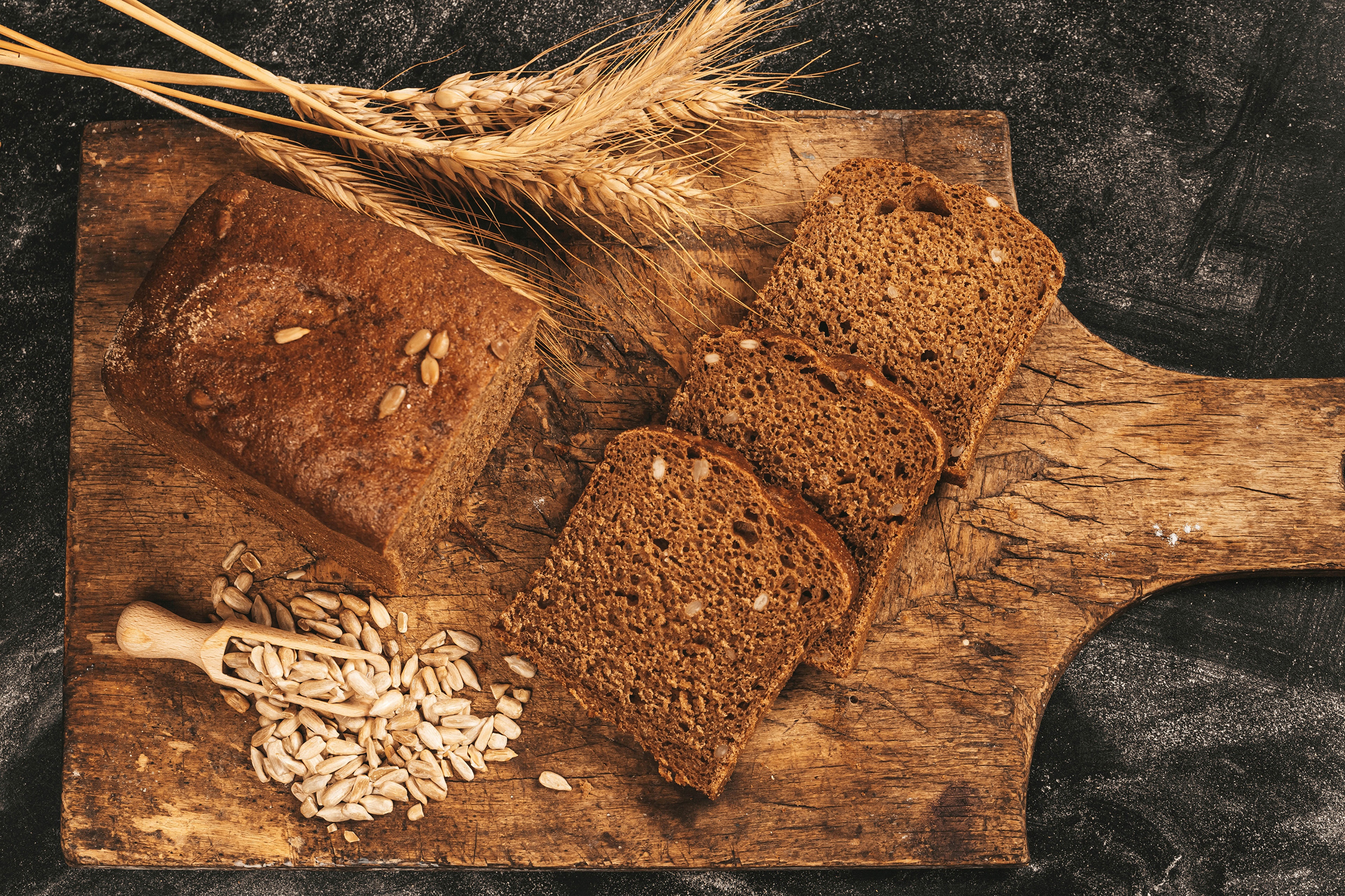 Bread, Sunflower Seeds, and Wheat on a Cutting Board HD Wallpaper