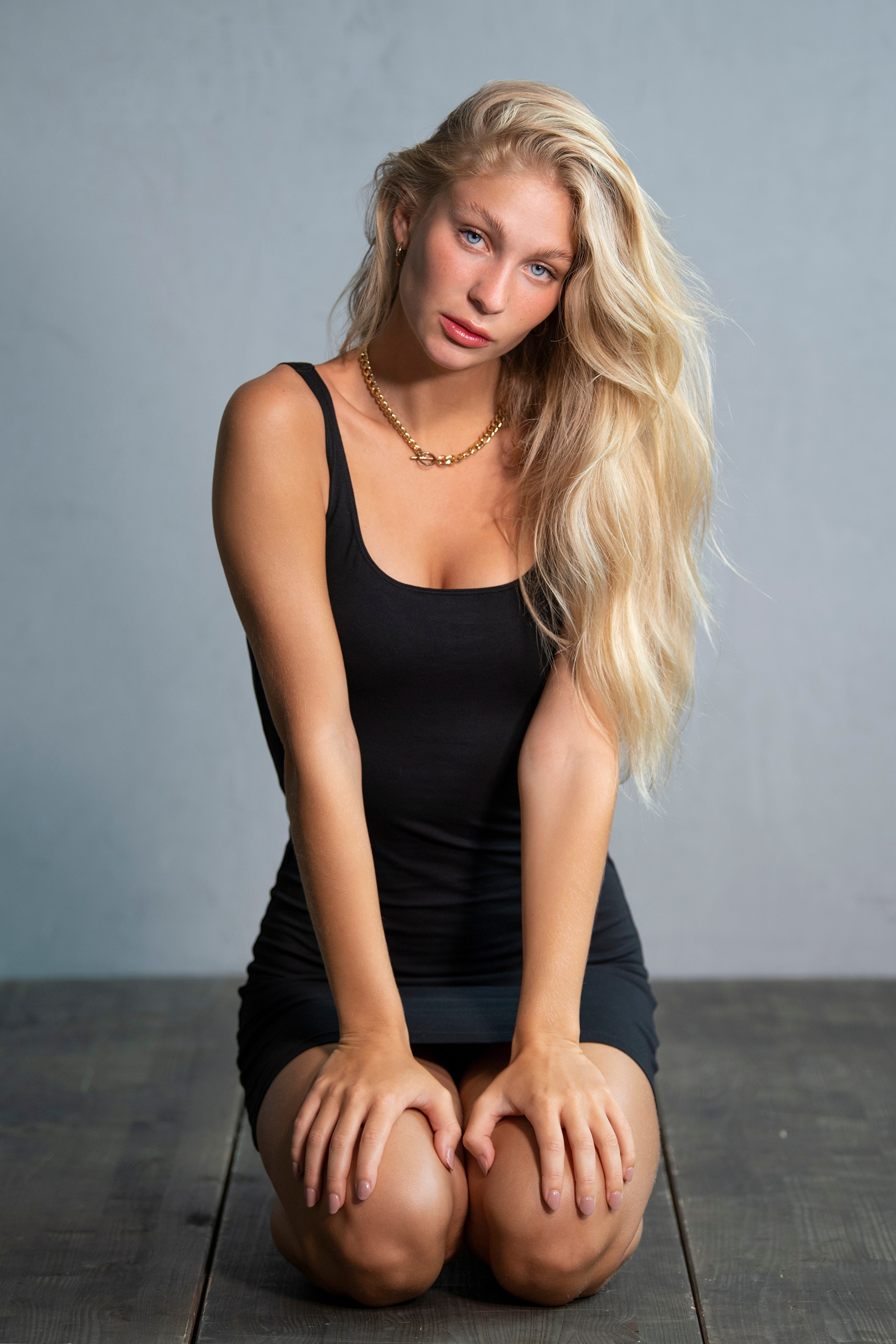 Blonde woman in black dress kneeling on wooden floor HD Phone Wallpaper