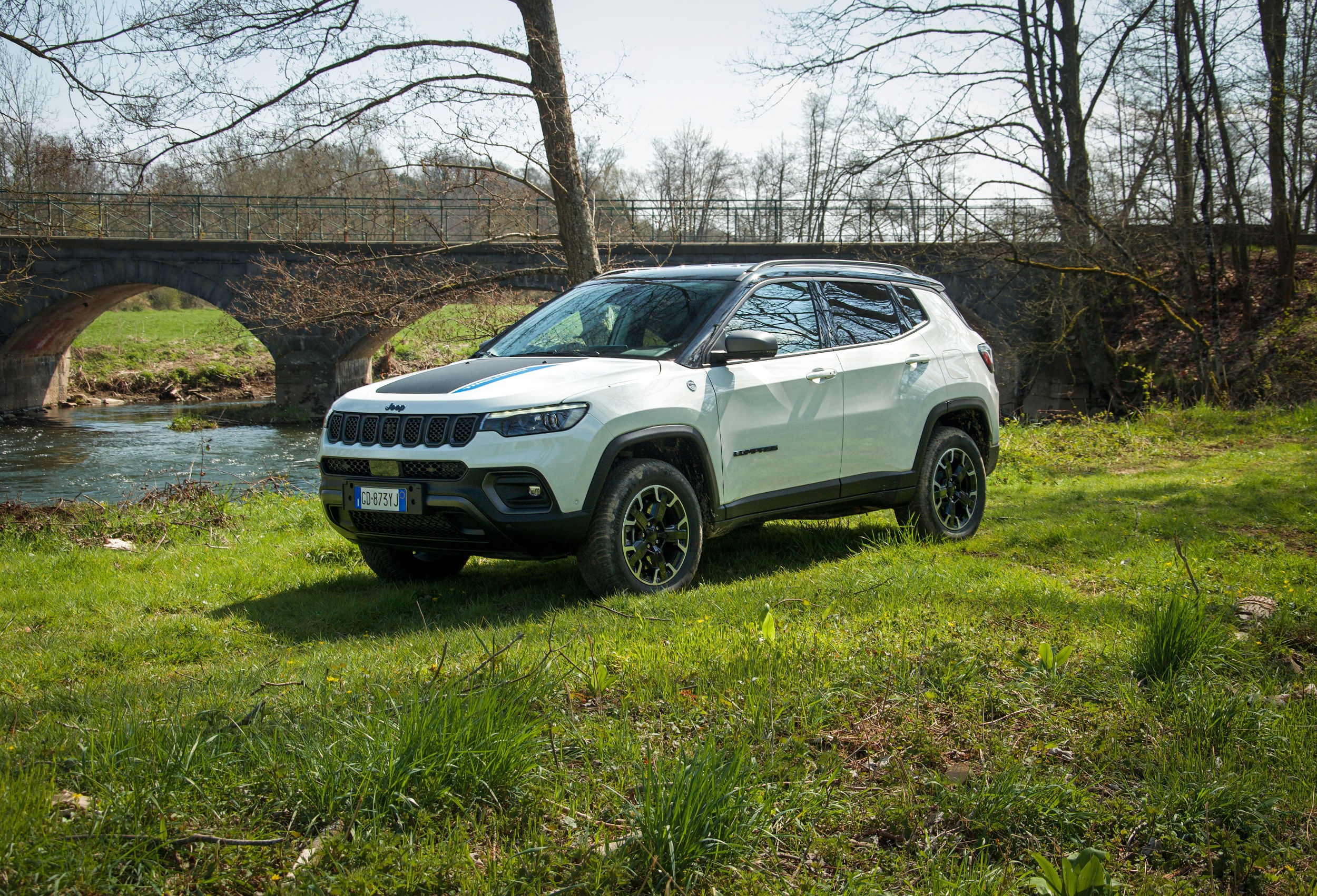 White Jeep Compass Trailhawk 4xe parked by a river and bridge HD Wallpaper