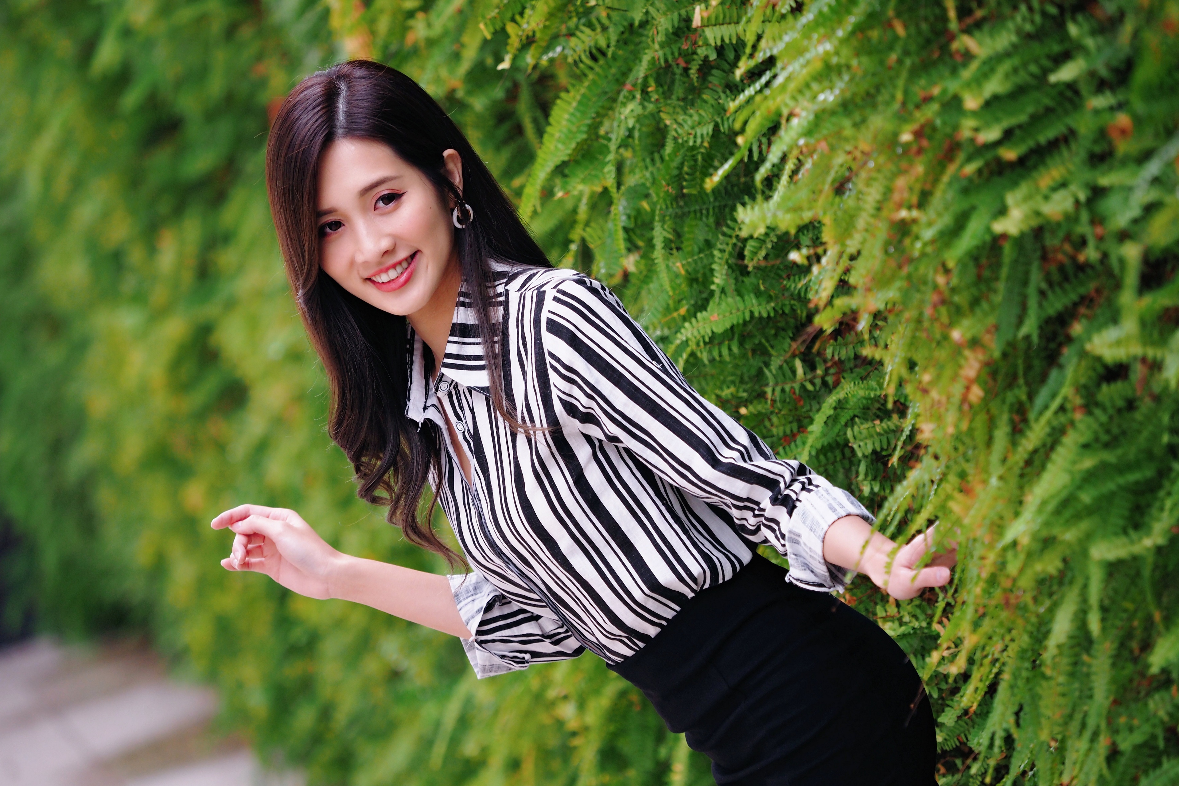 Asian woman in striped shirt near green shrubs HD Wallpaper