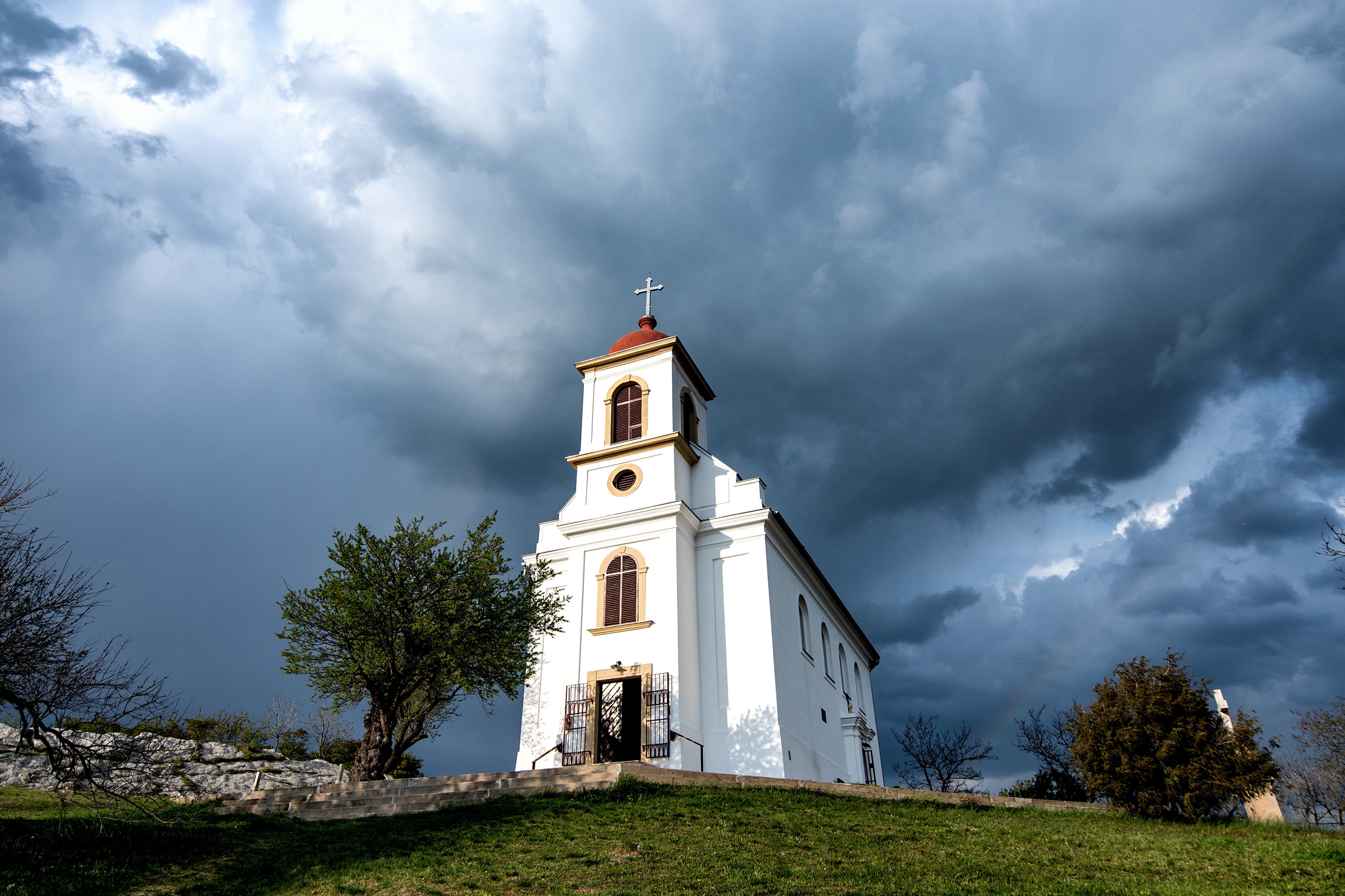 White church with red roof under stormy clouds in Hungary HD Wallpaper