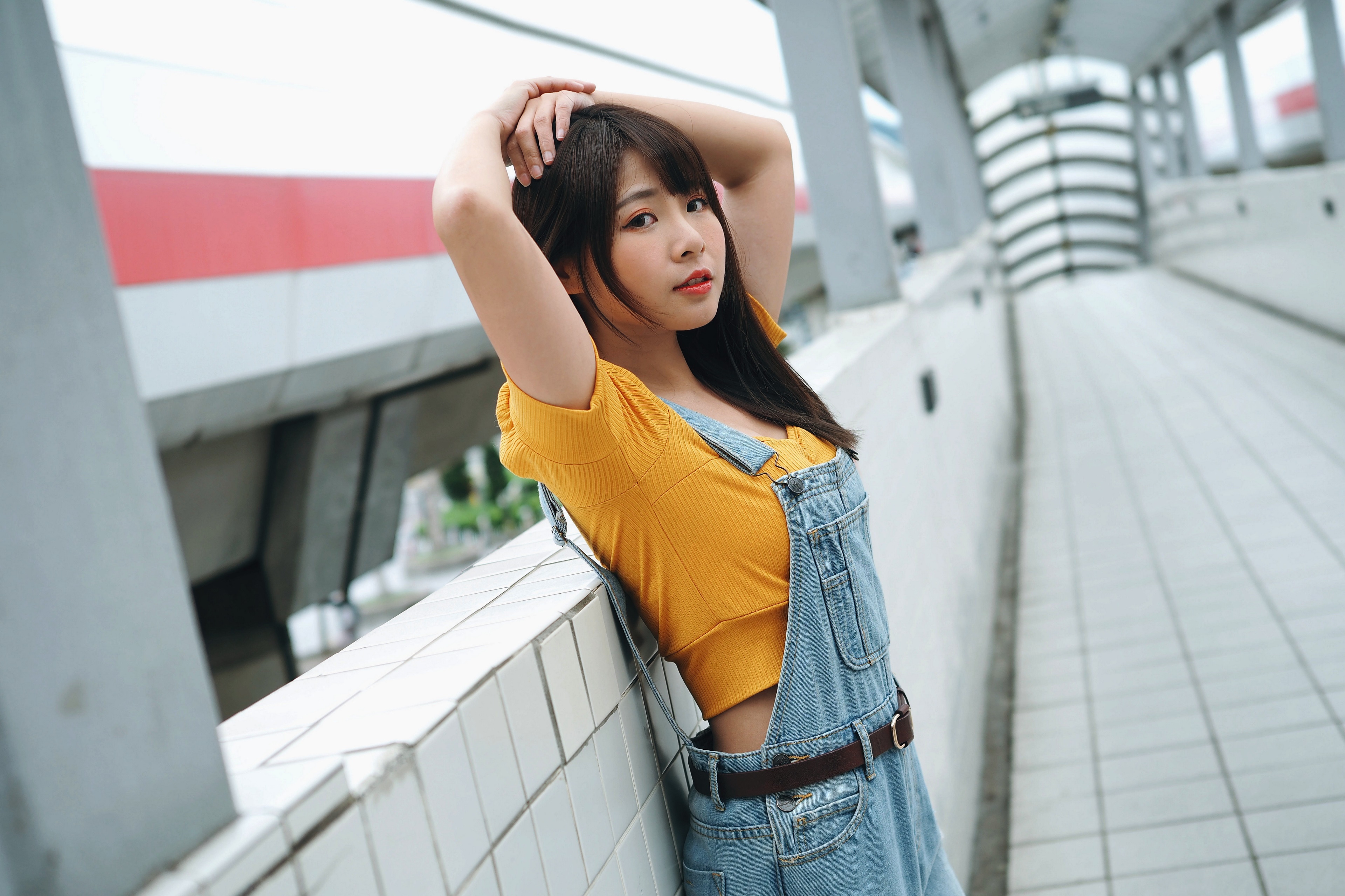 Asian woman in yellow top and denim overalls posing HD Wallpaper