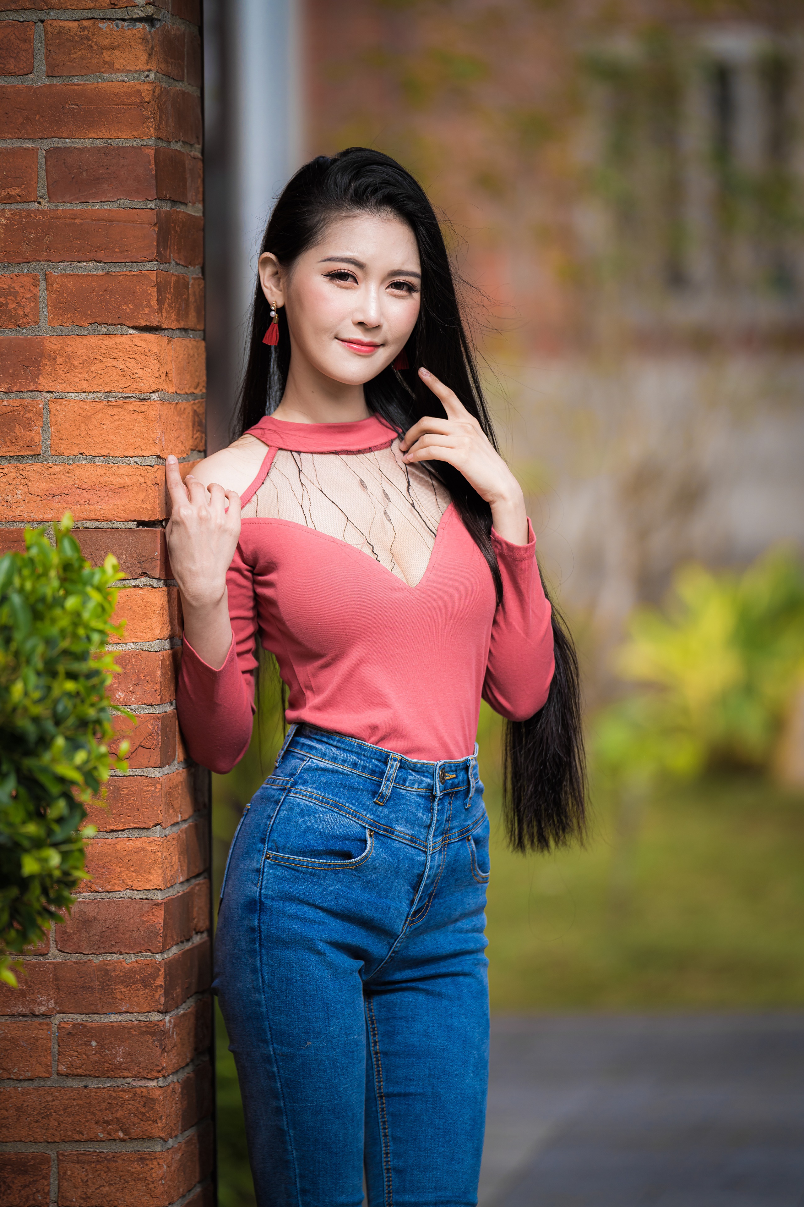 Asian woman in pink top and jeans posing by brick wall HD Phone Wallpaper
