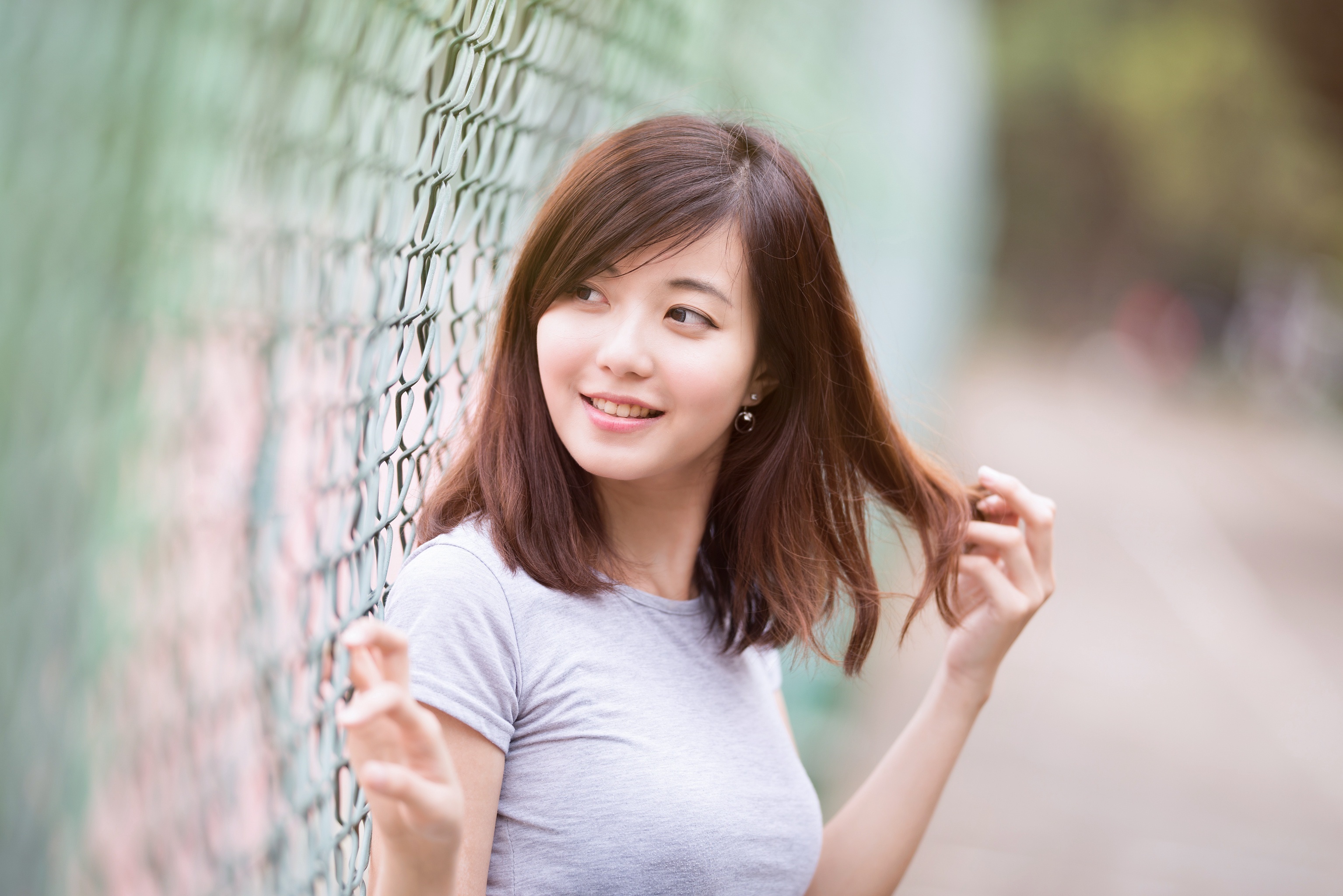 Asian woman with brown hair smiling near a fence HD Wallpaper