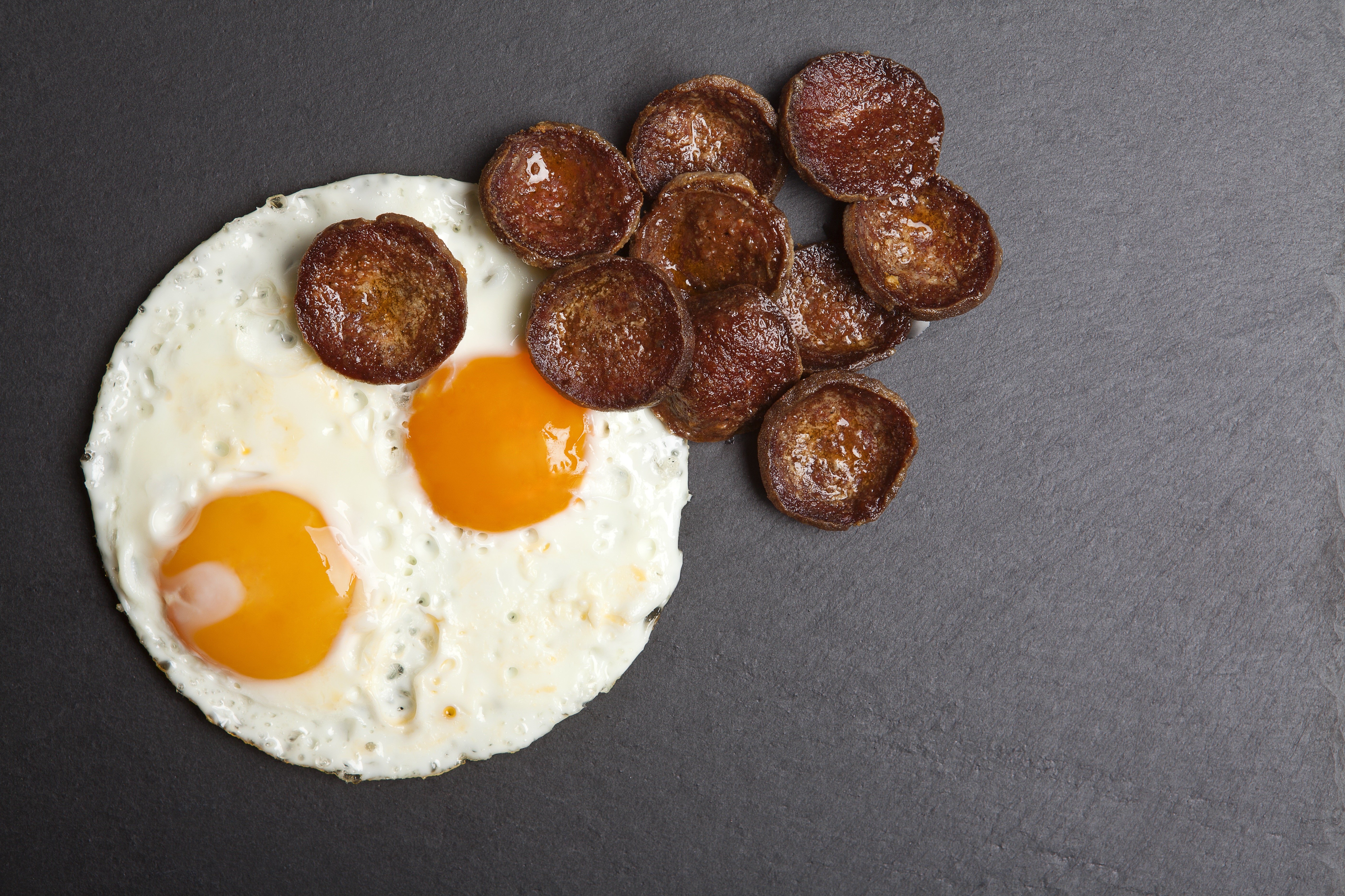 Fried eggs and sausage slices on gray background HD Wallpaper