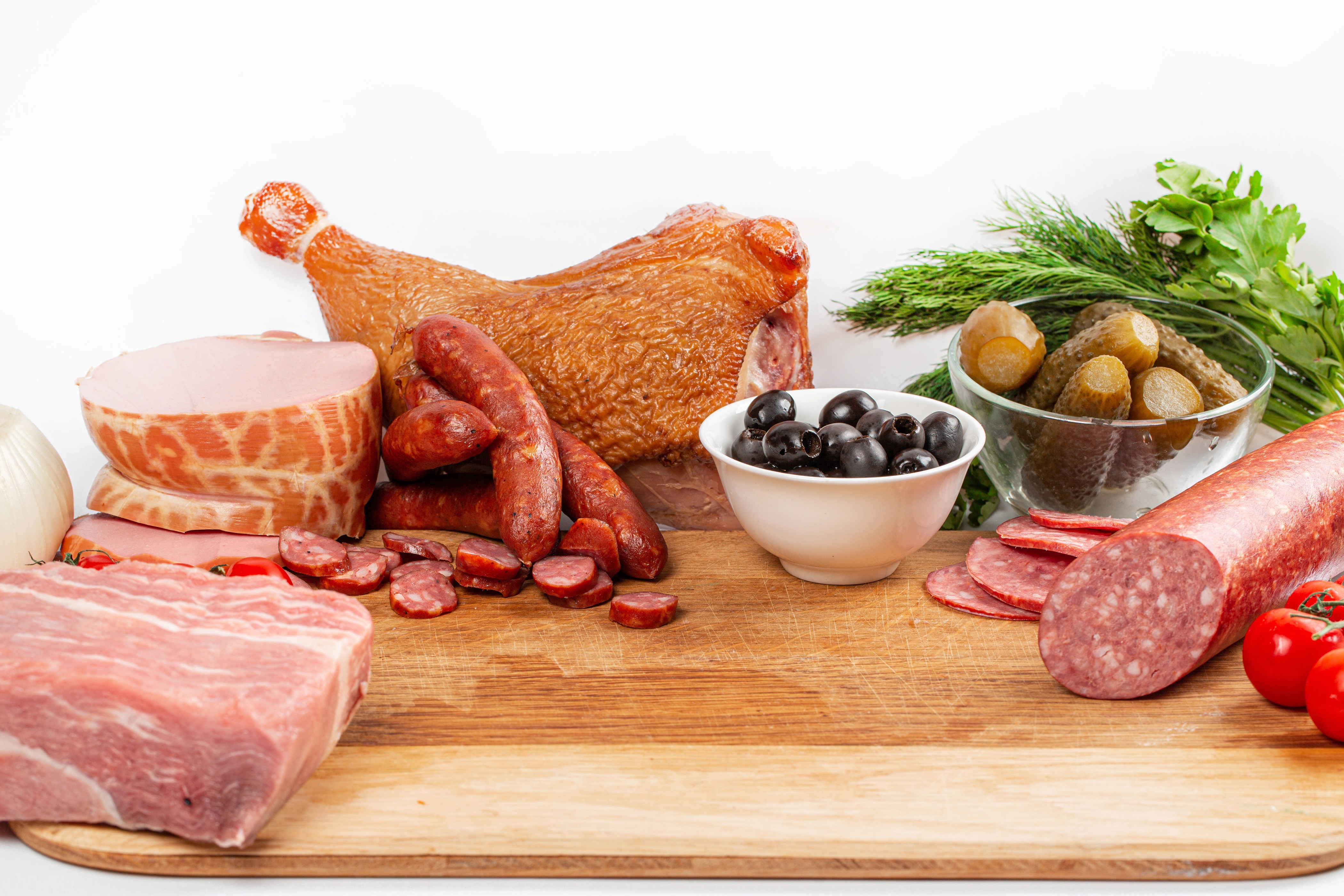 Meat products, sausages, ham, olives, pickles, and tomatoes on a cutting board HD Wallpaper