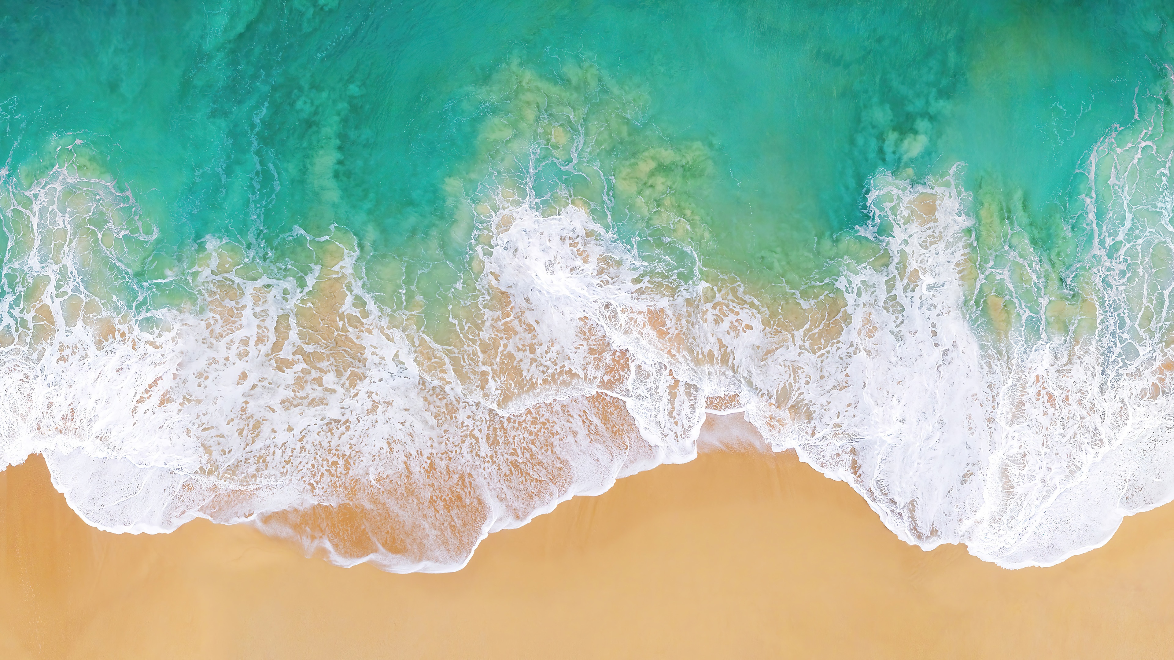 Aerial view of ocean waves crashing on a sandy beach HD Wallpaper