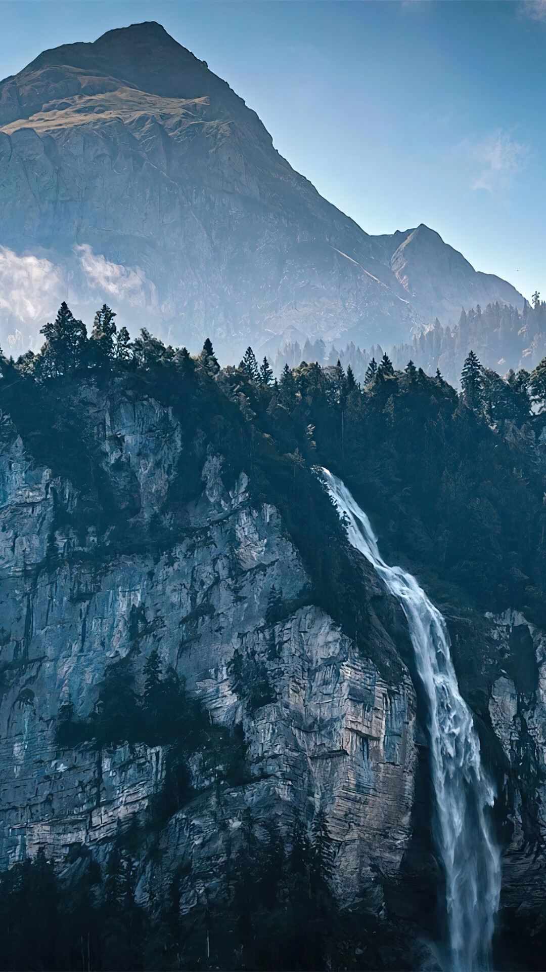 Waterfall cascading down a rocky mountain face with a peak in the background HD Phone Wallpaper