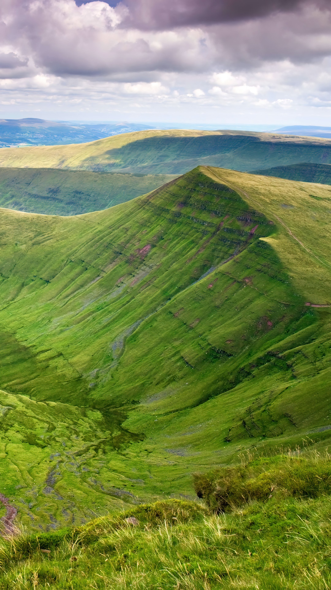 Green rolling hills and mountains under a cloudy sky HD Phone Wallpaper