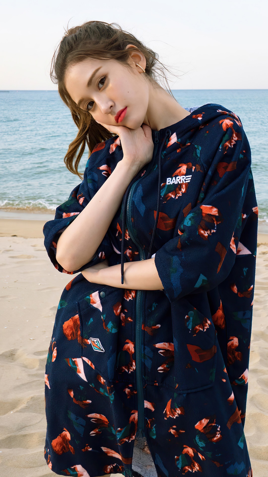 Jeon Somi posing on a beach in a floral hoodie HD Phone Wallpaper