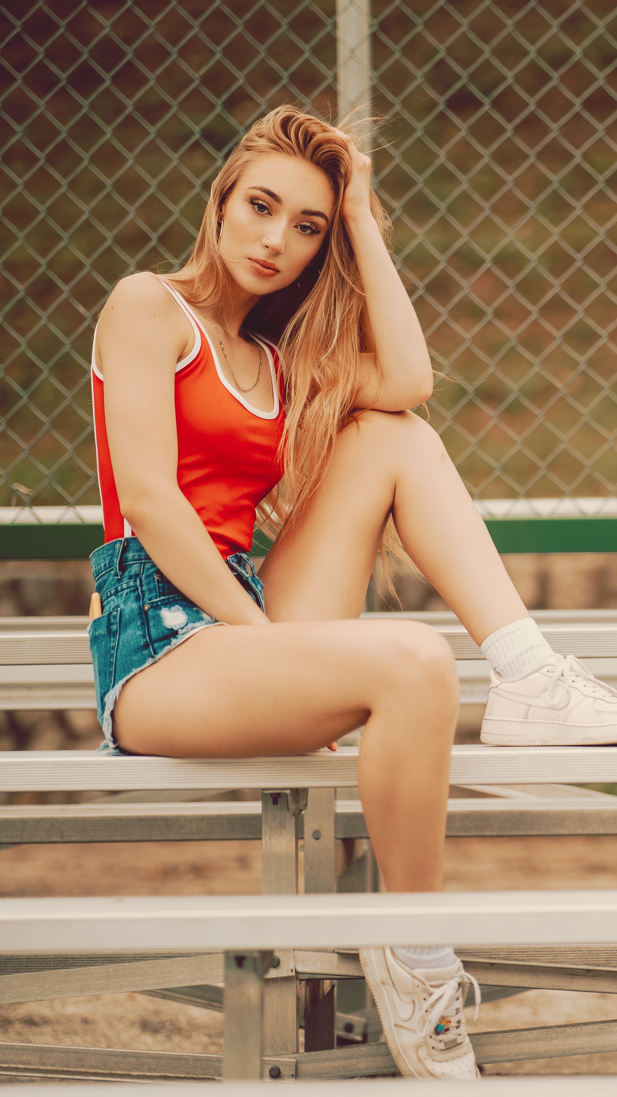 Model in red top and denim shorts on bleachers HD Phone Wallpaper