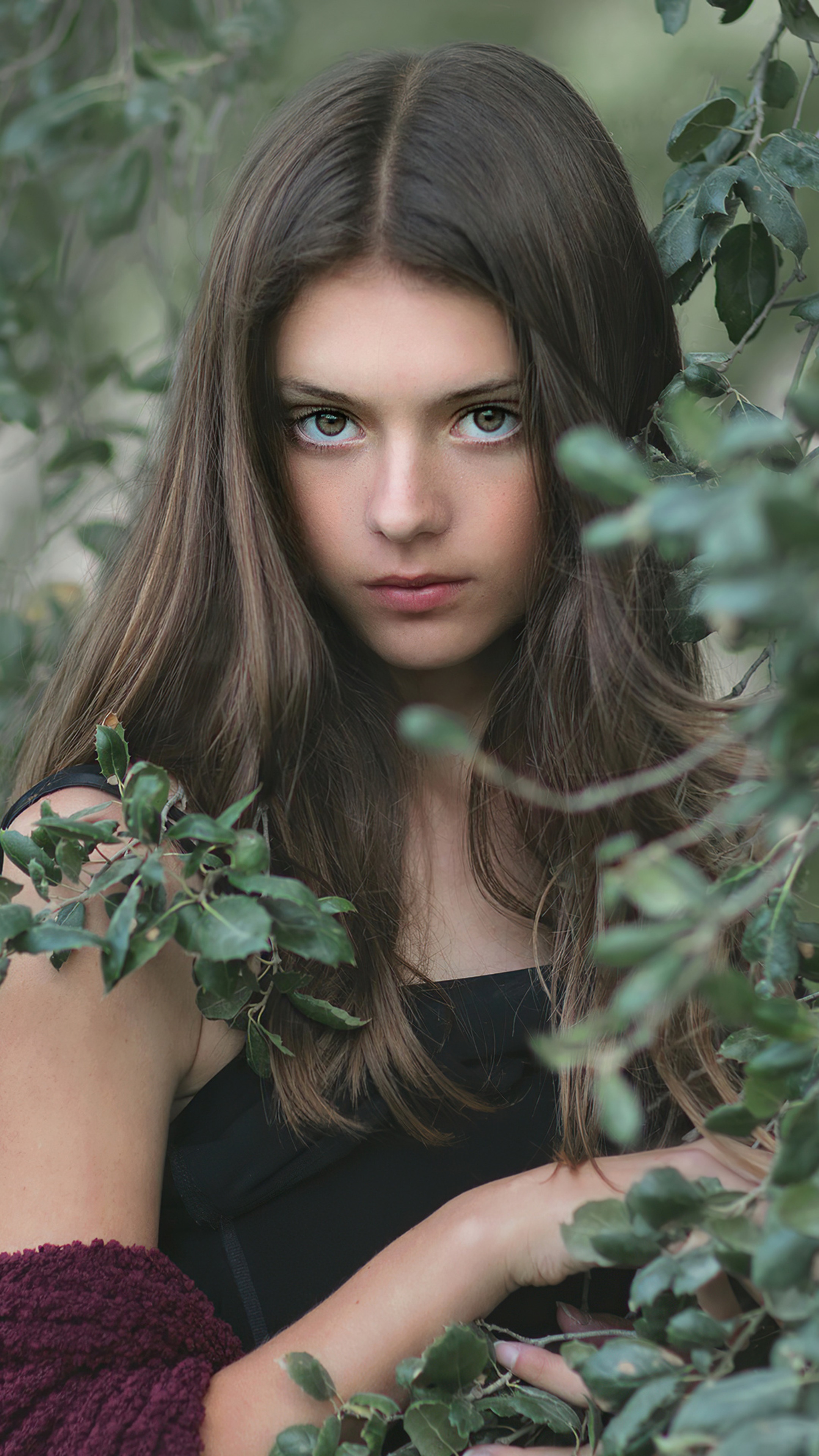 Young girl with long brown hair among green leaves HD Phone Wallpaper