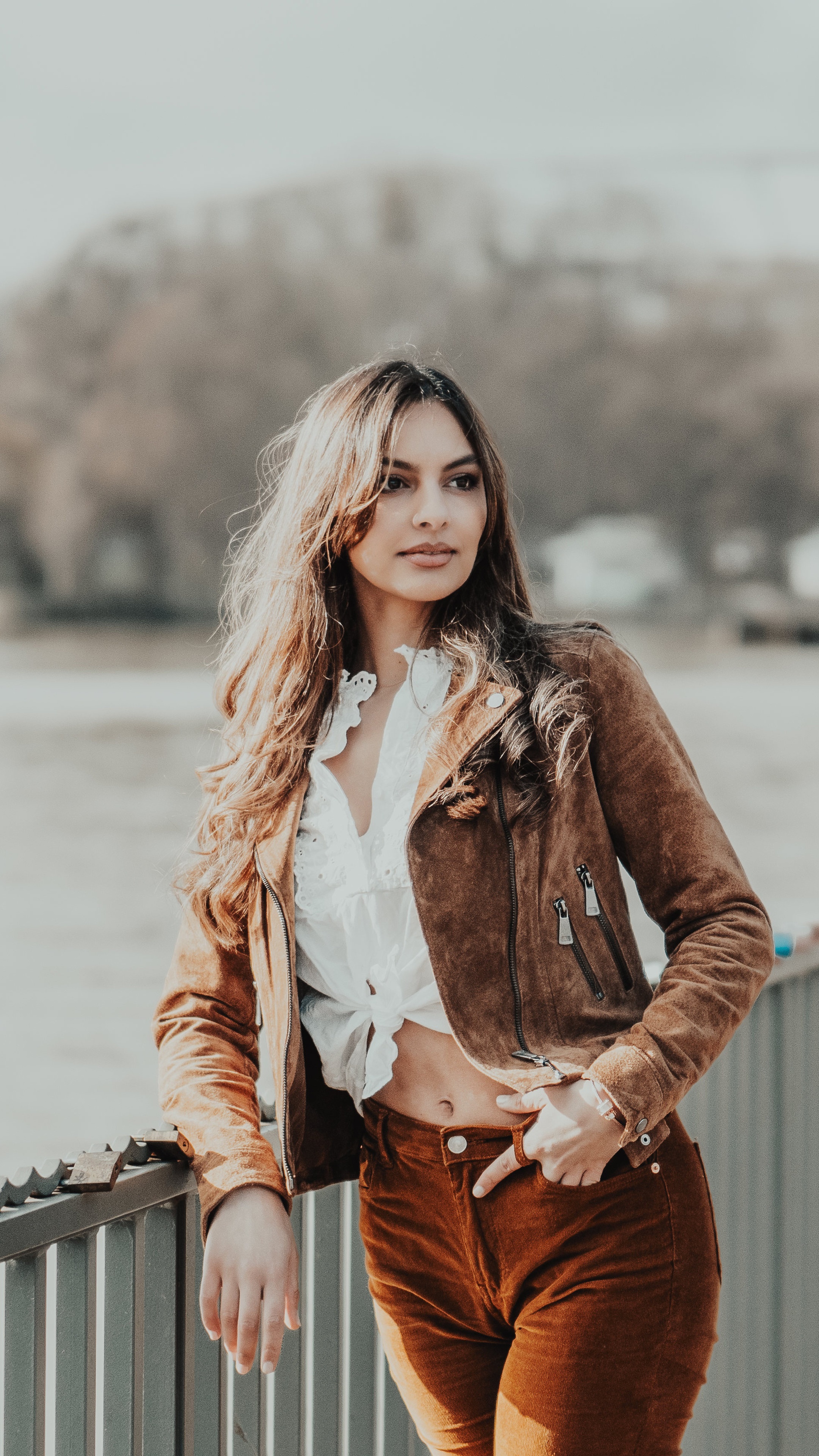 Woman in brown jacket and orange pants by a railing HD Phone Wallpaper