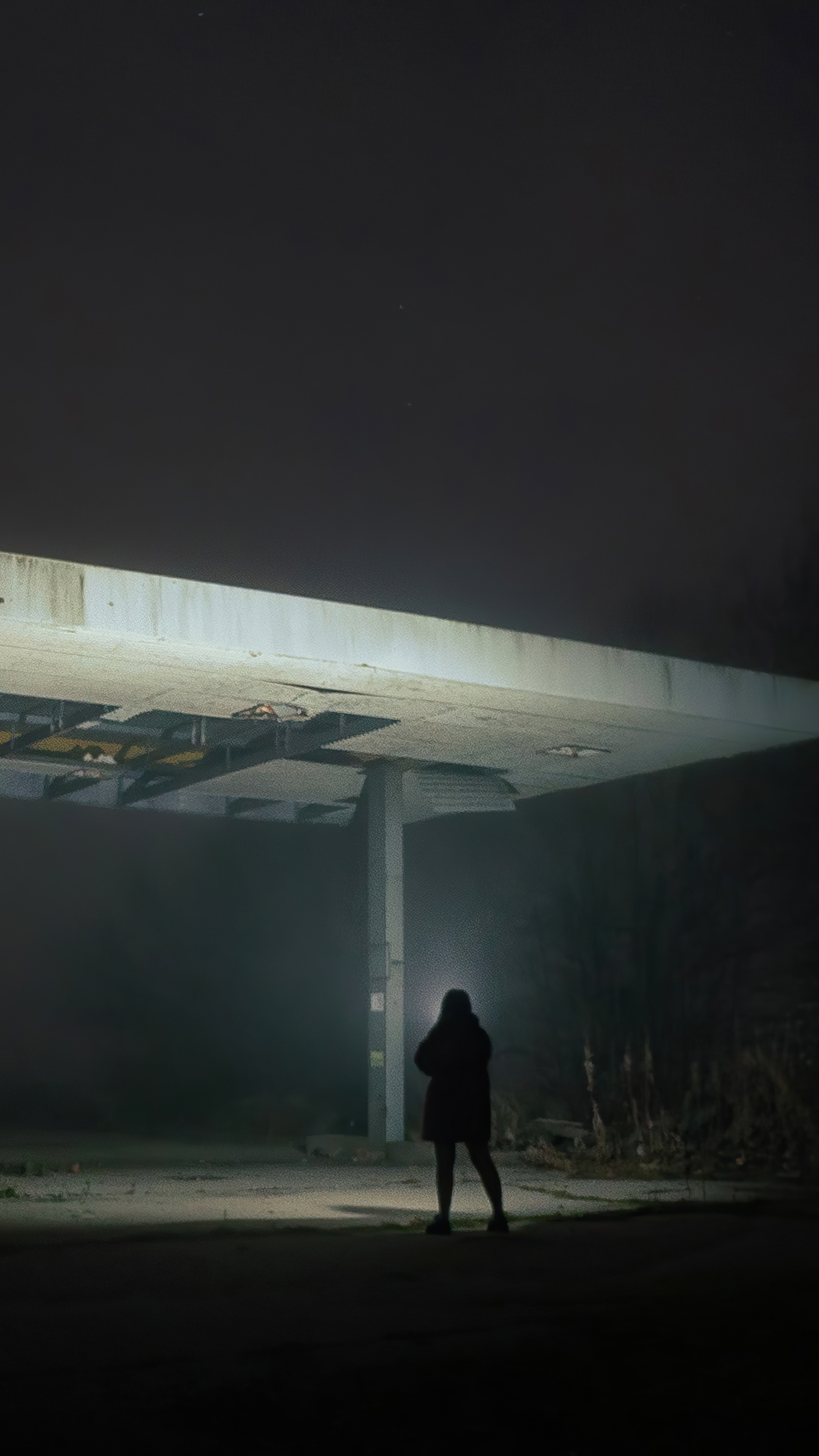 Person standing under a damaged overpass at night HD Phone Wallpaper