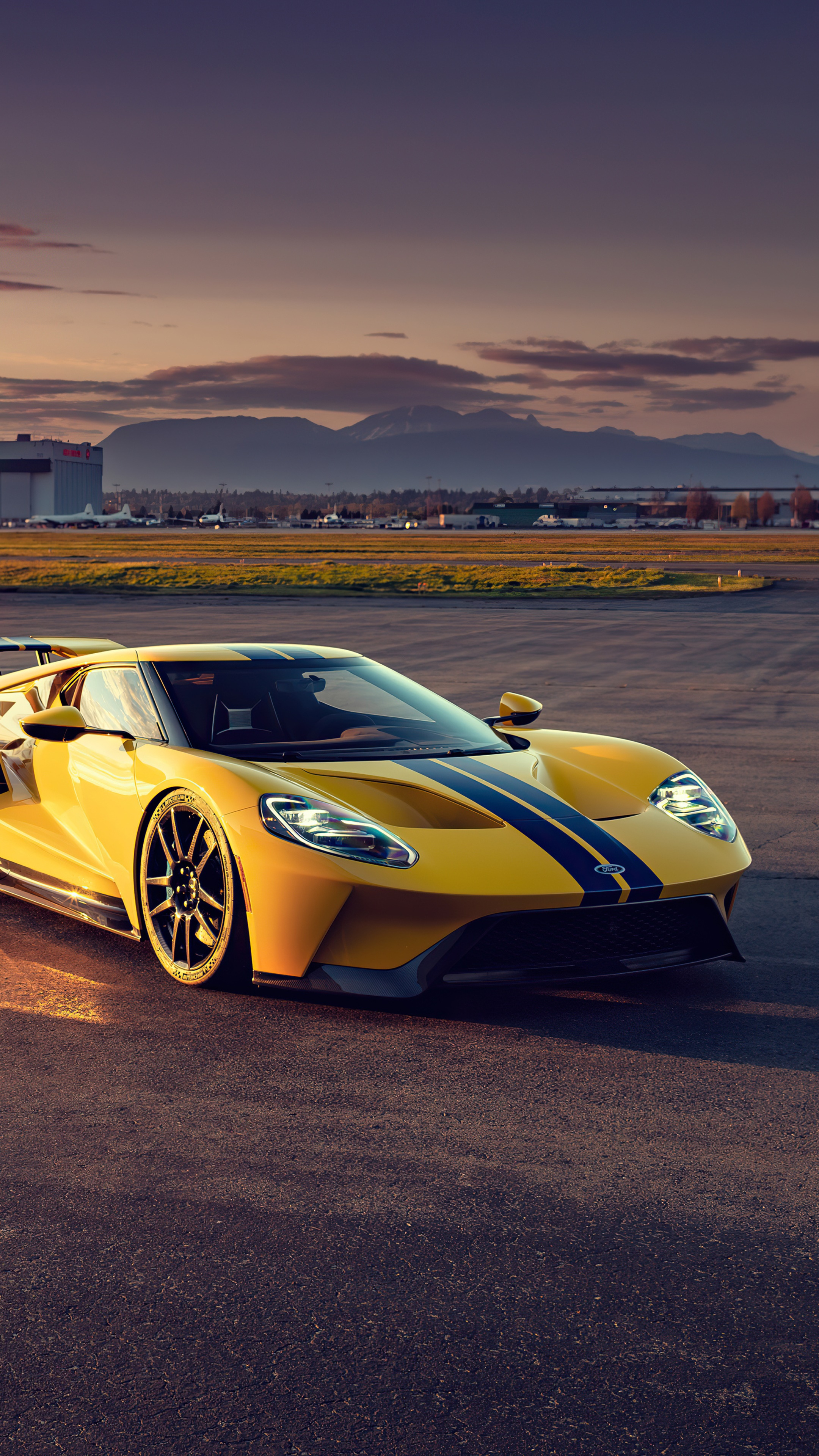 Yellow Ford GT with blue stripes on tarmac HD Phone Wallpaper