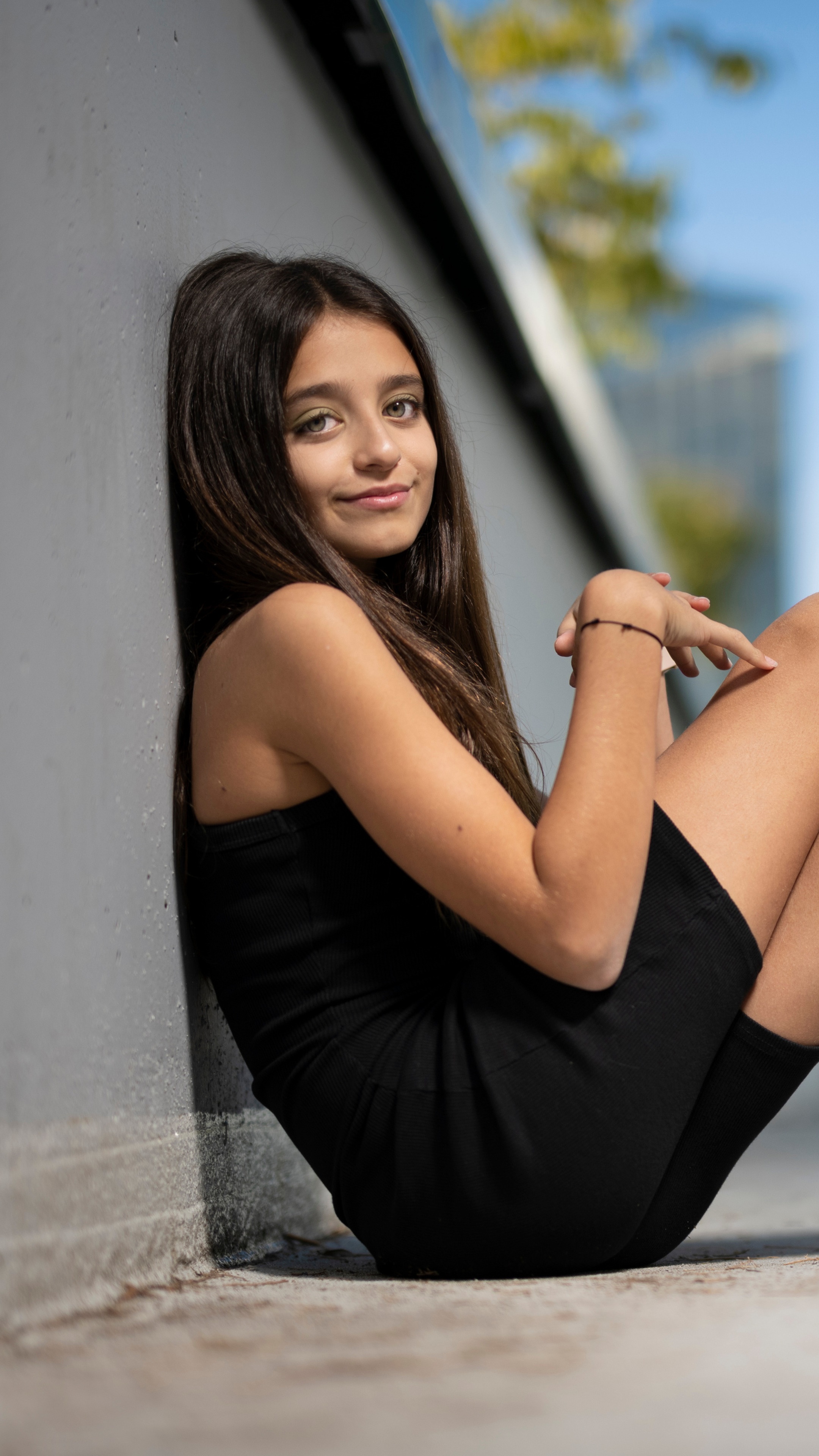 Young girl in a black dress leaning against a wall HD Phone Wallpaper