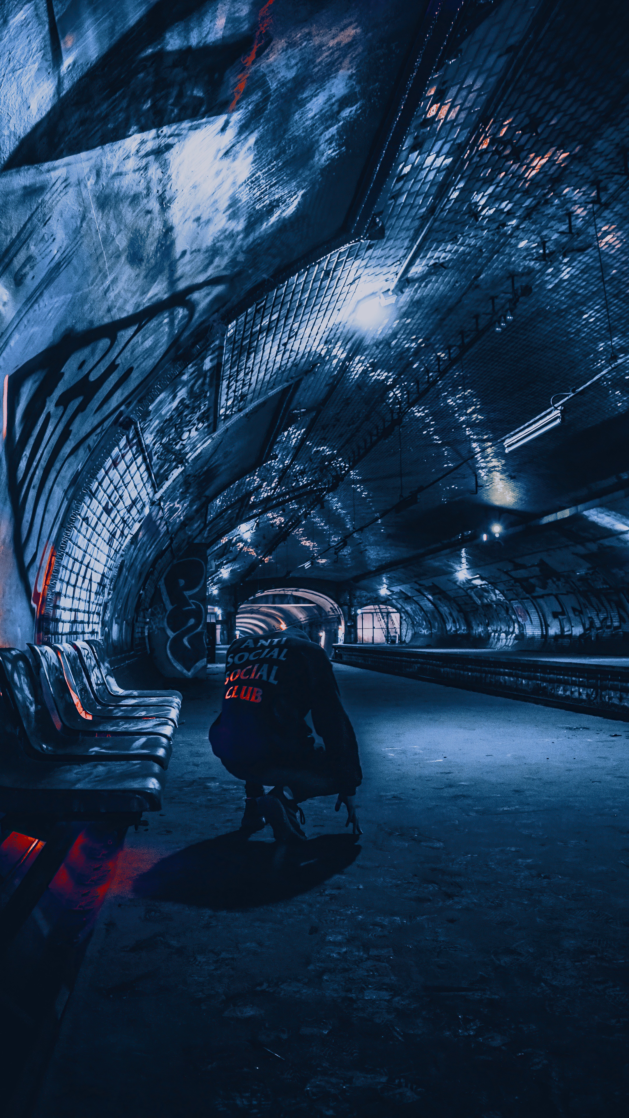 Person in hoodie crouching in a dark subway tunnel HD Phone Wallpaper