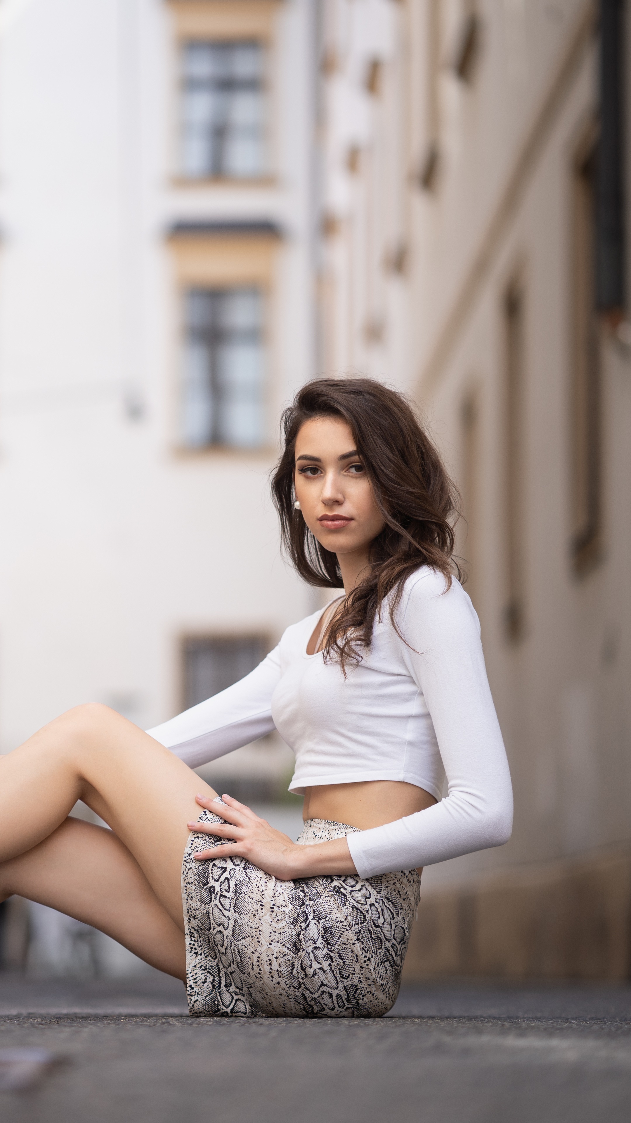 Model in white top and snake print skirt sitting on ground HD Phone Wallpaper