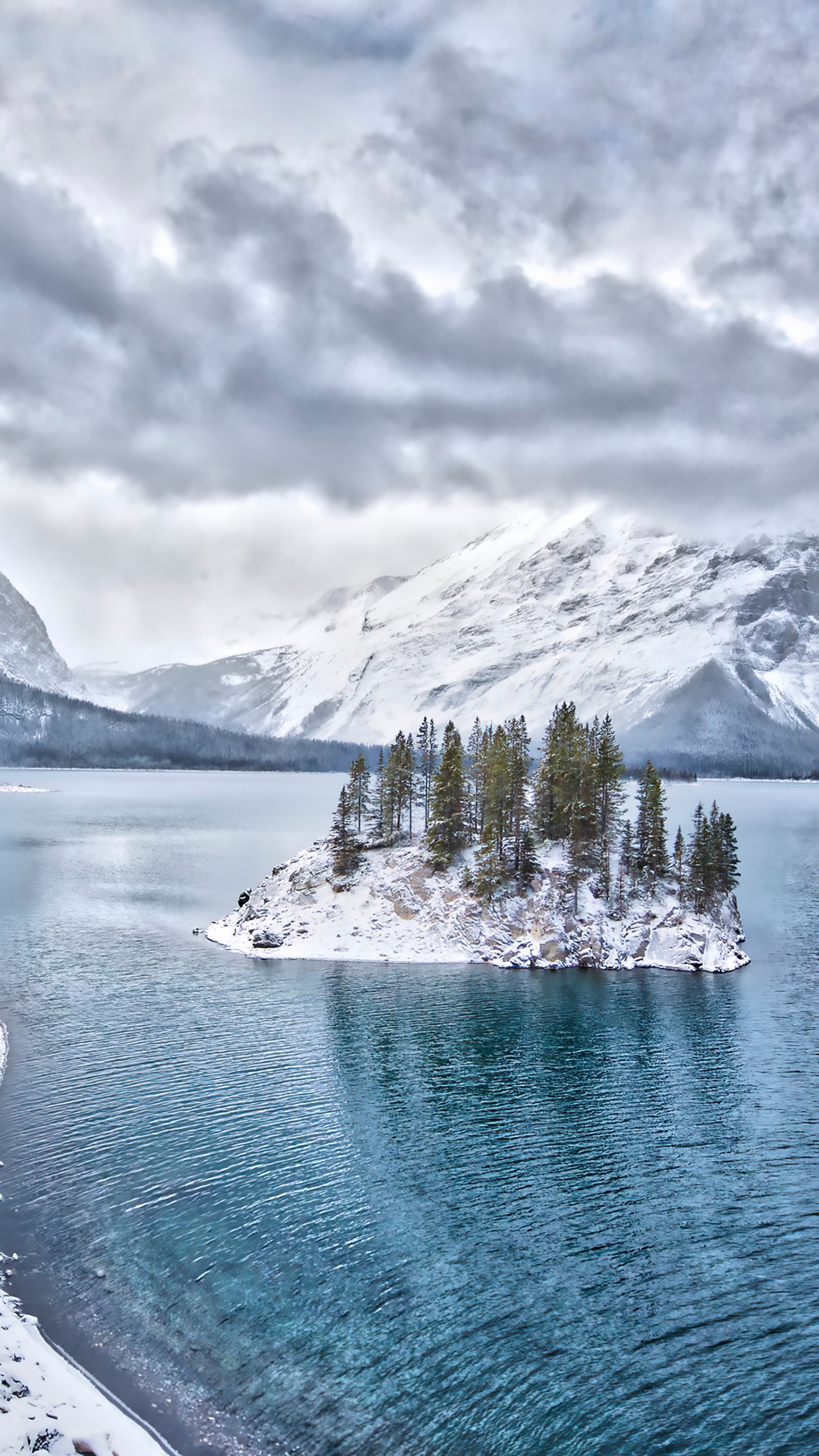 Winter island with trees on a lake with snowy mountains HD Phone Wallpaper