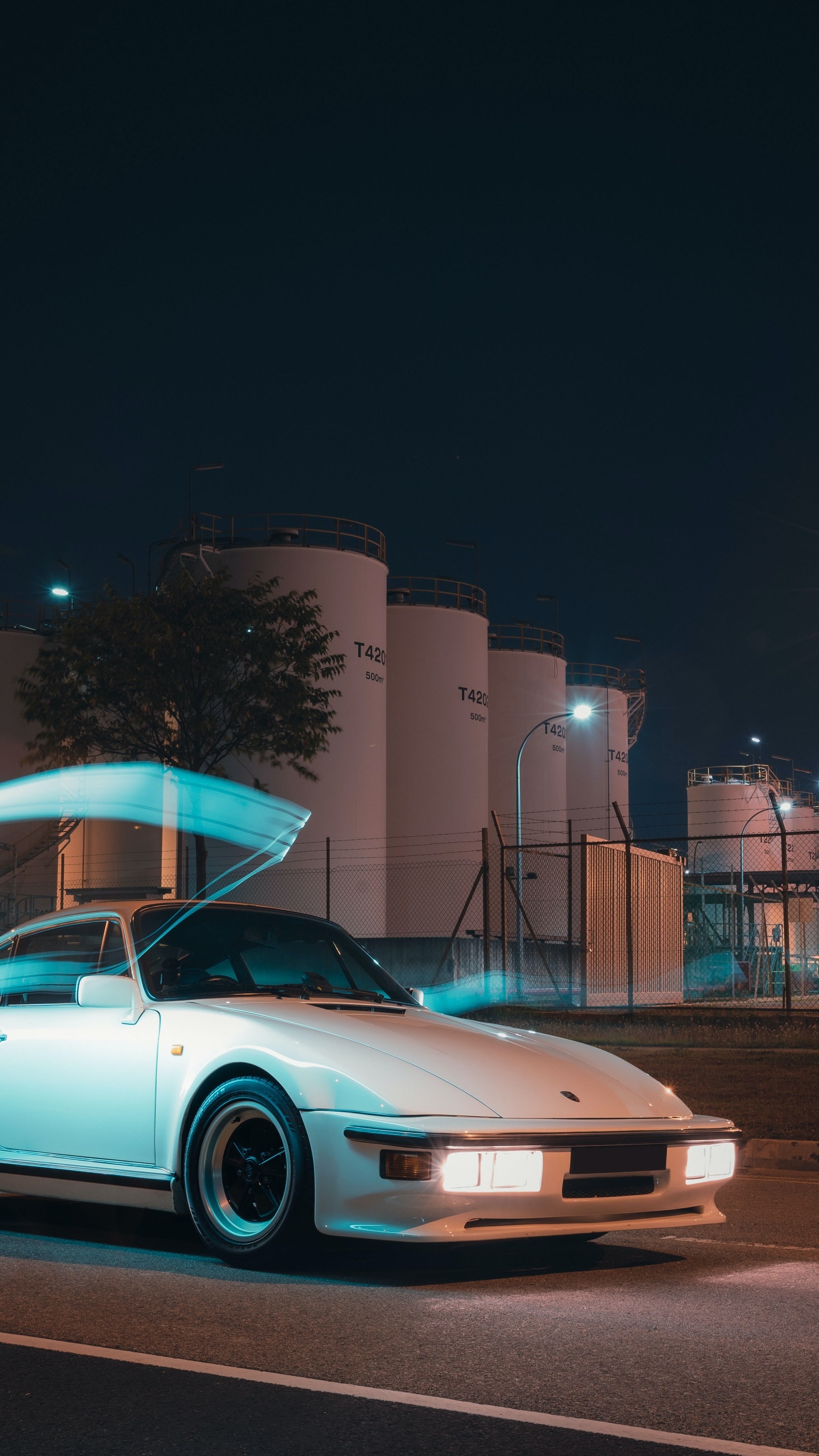 White Porsche 911 at night with industrial tanks HD Phone Wallpaper