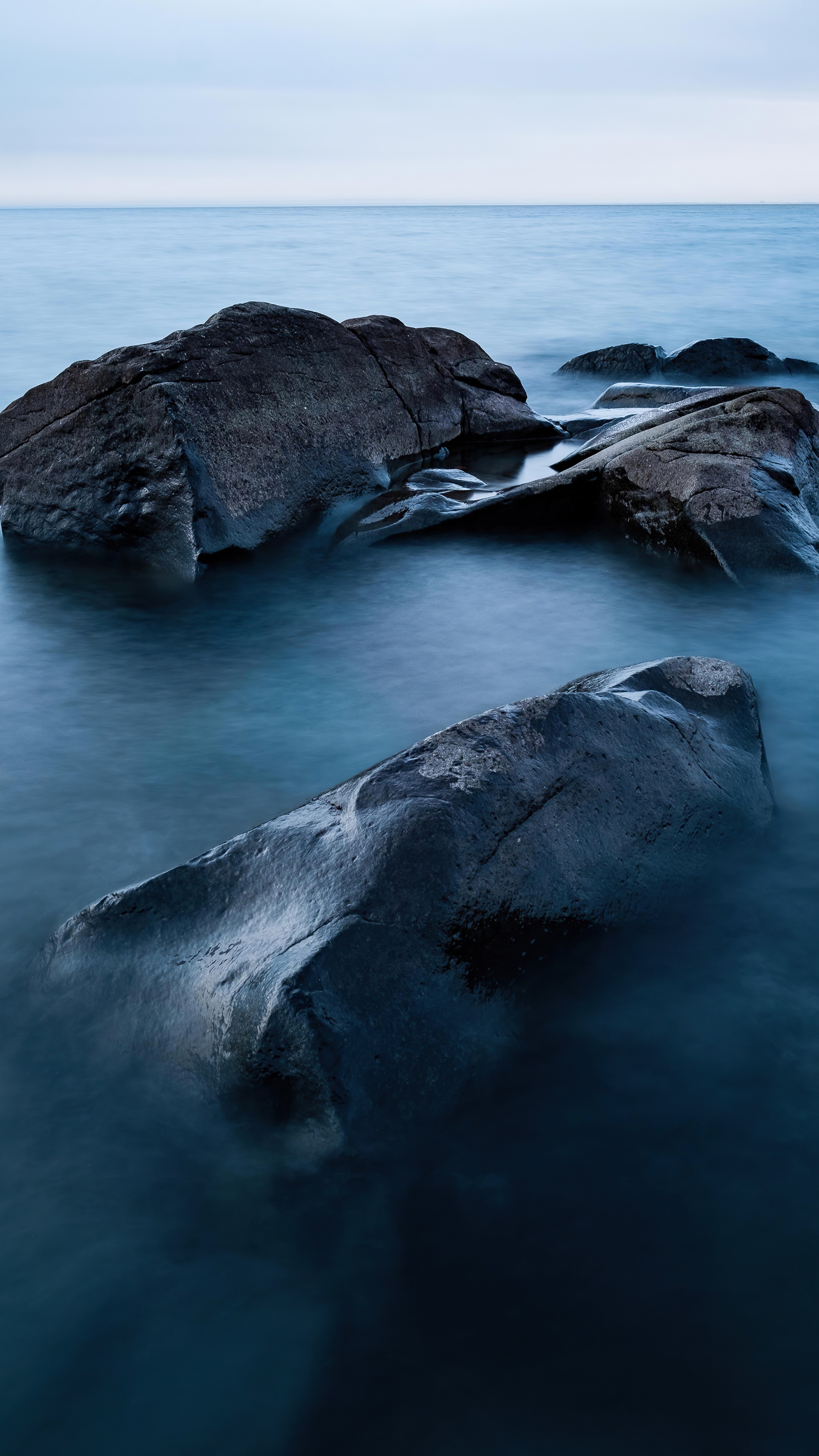 Dark rocks in calm blue water HD Phone Wallpaper