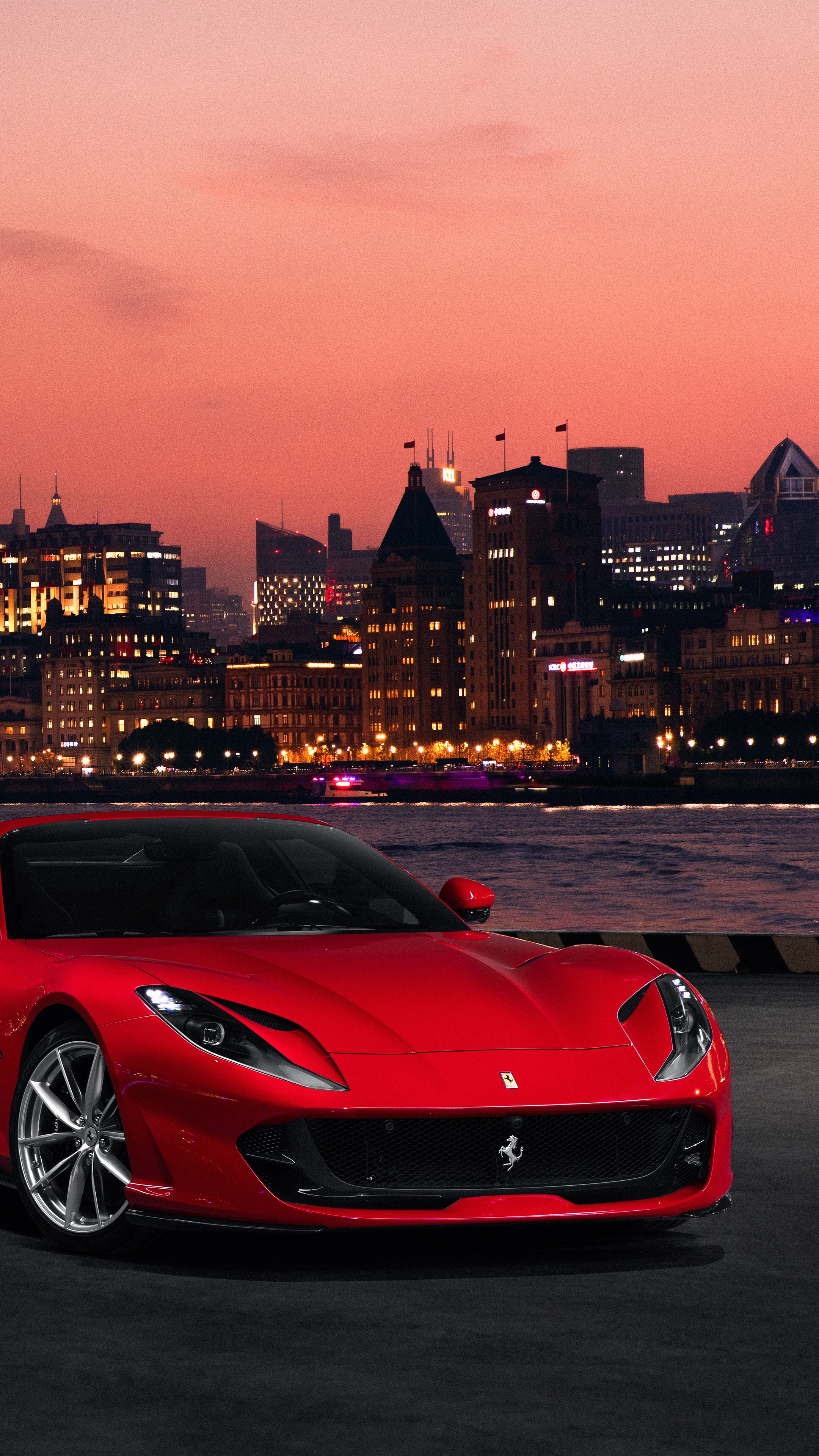 Red Ferrari 812 Superfast in front of city skyline at dusk HD Phone Wallpaper