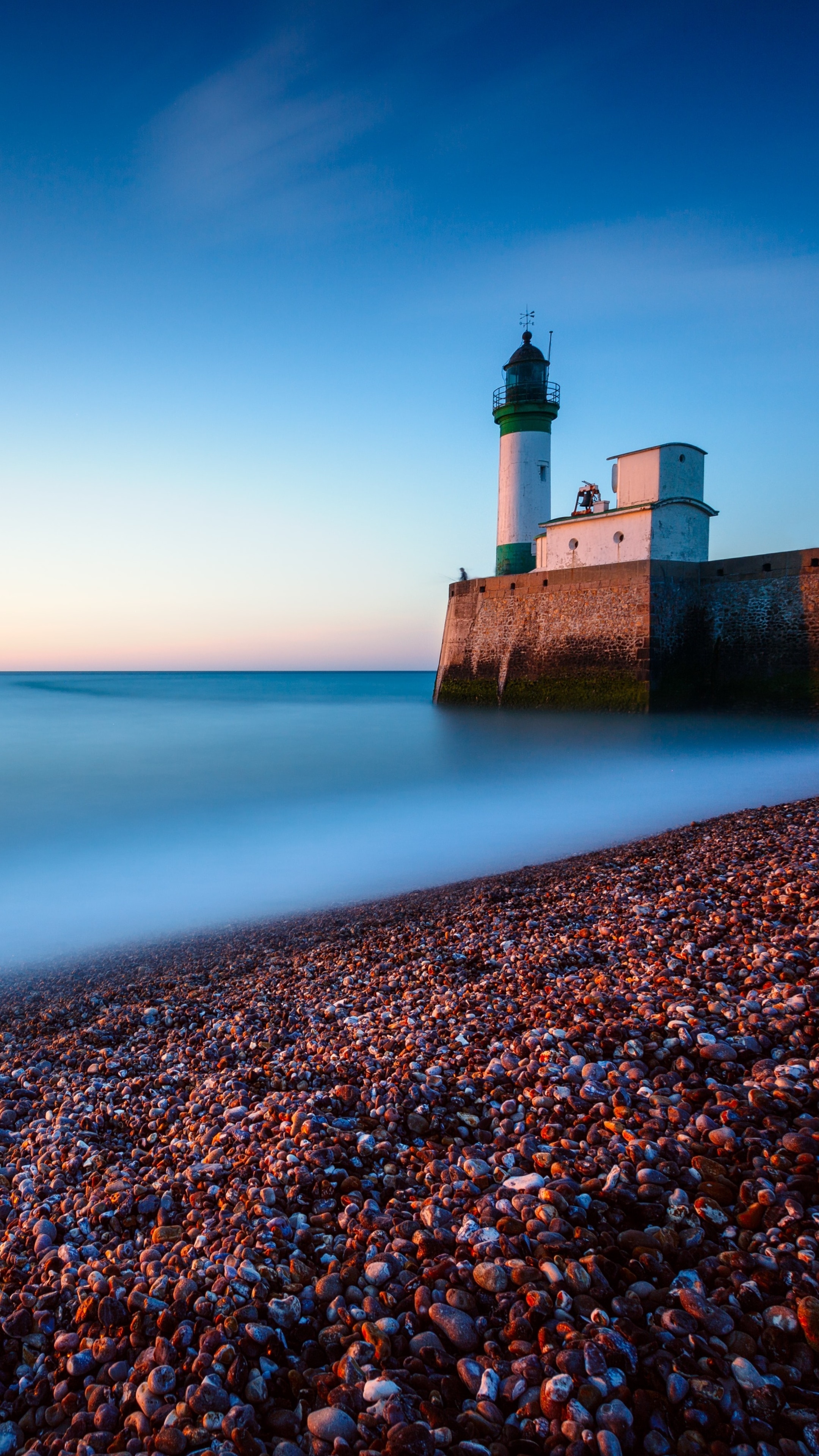 Lighthouse on a stone pier by the ocean at dusk HD Phone Wallpaper