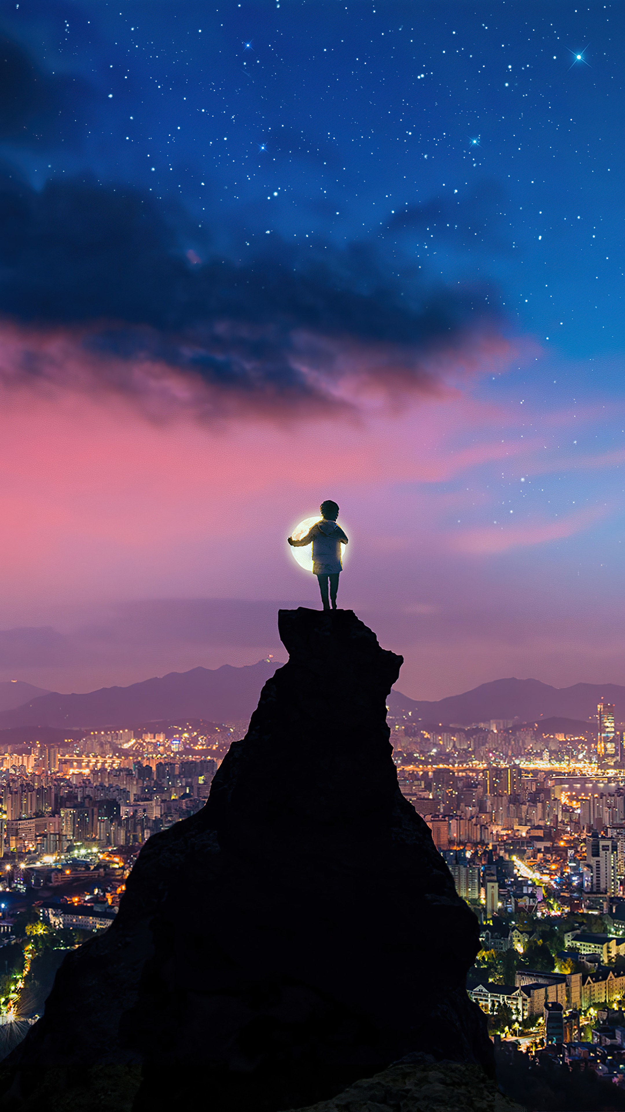 Child holding a glowing orb on a mountain peak overlooking a city at night HD Phone Wallpaper