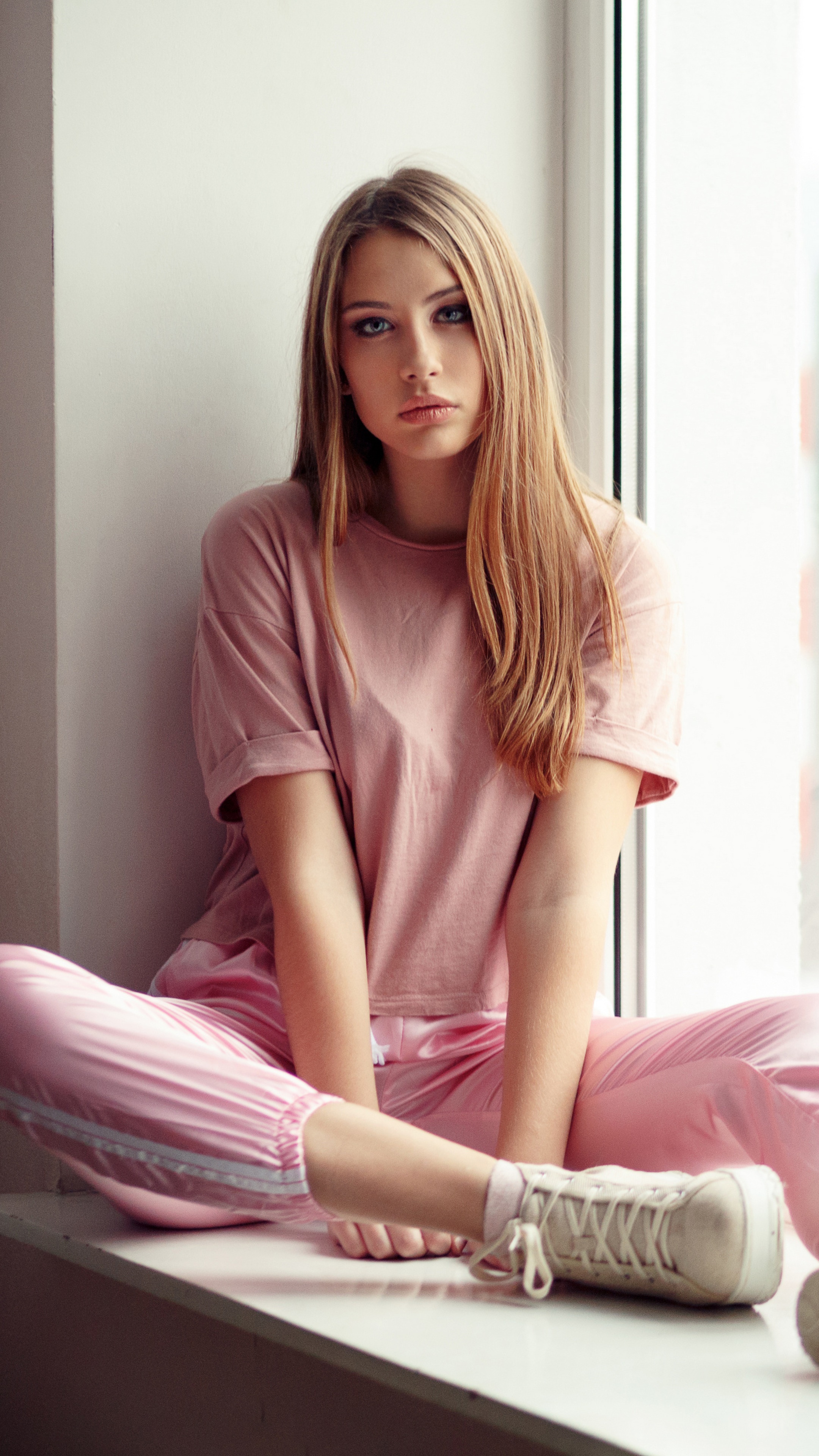 Young woman in pink loungewear sitting by window HD Phone Wallpaper