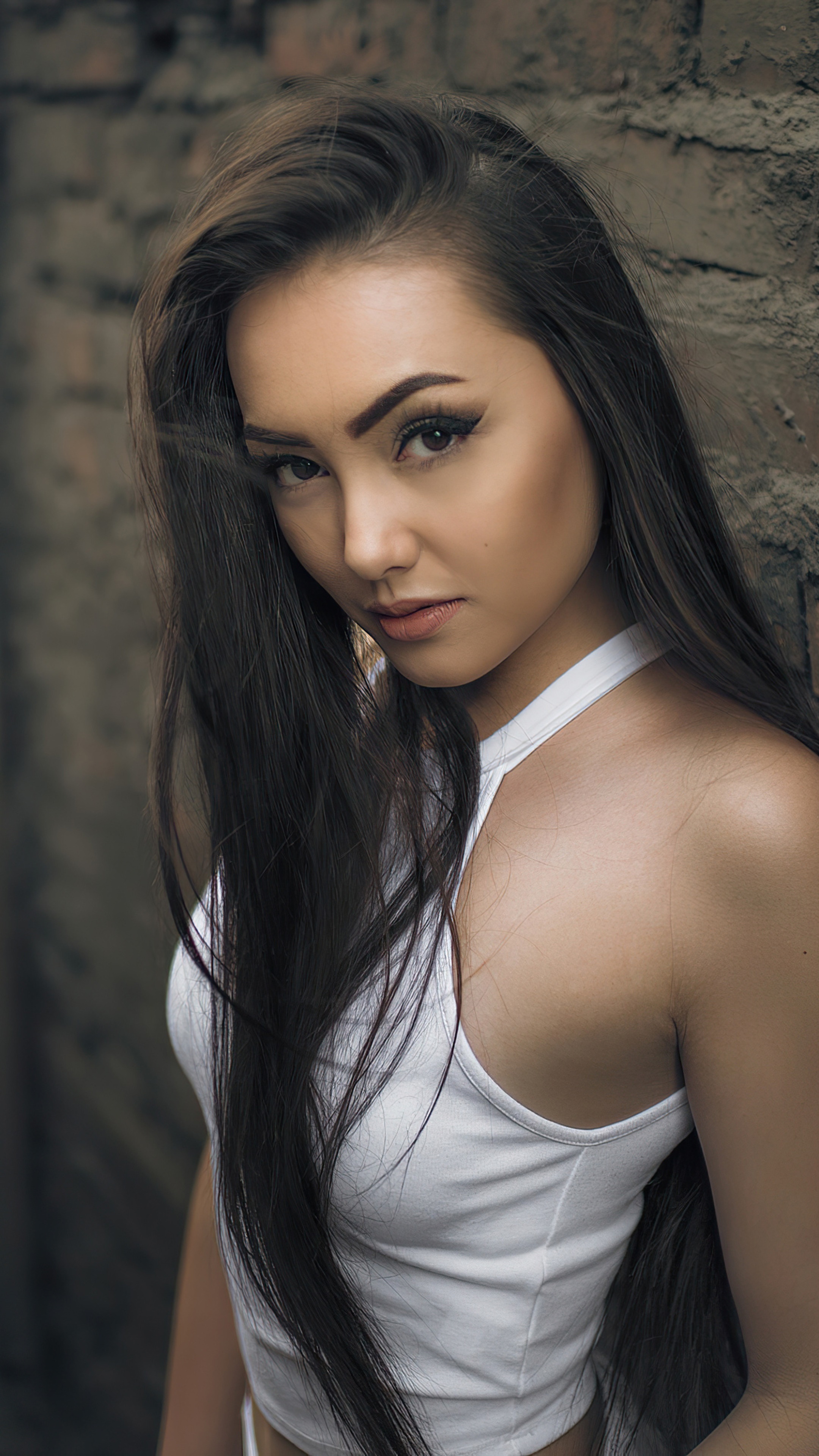 Woman with long dark hair leaning against a brick wall HD Phone Wallpaper