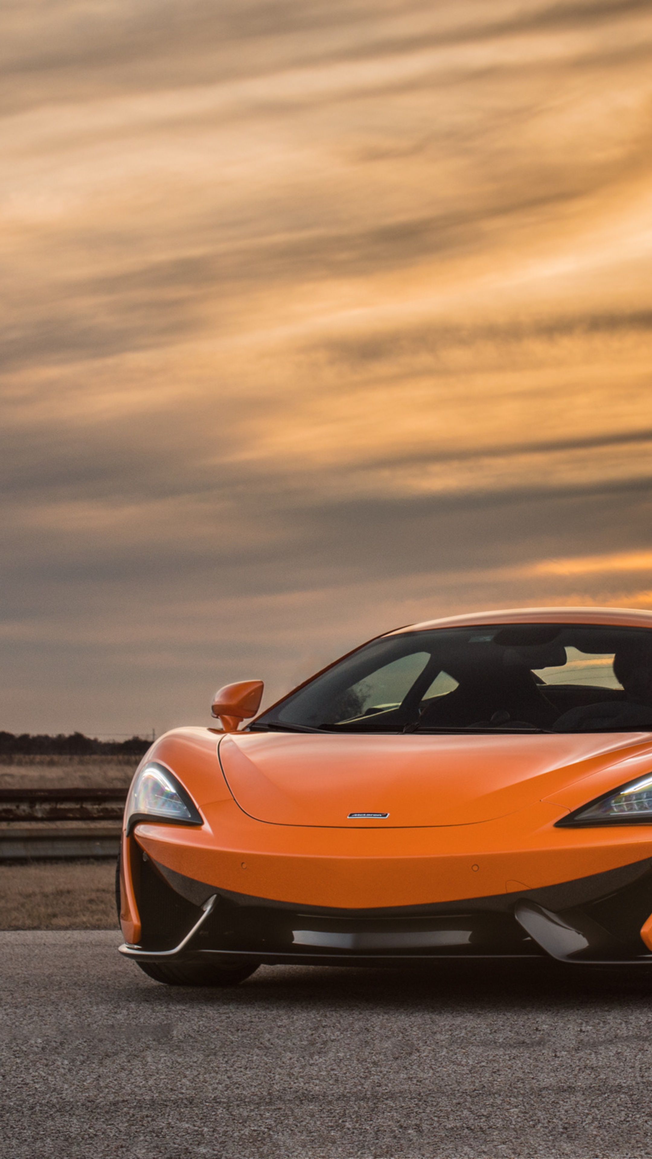 Orange McLaren sports car on a road at sunset HD Phone Wallpaper