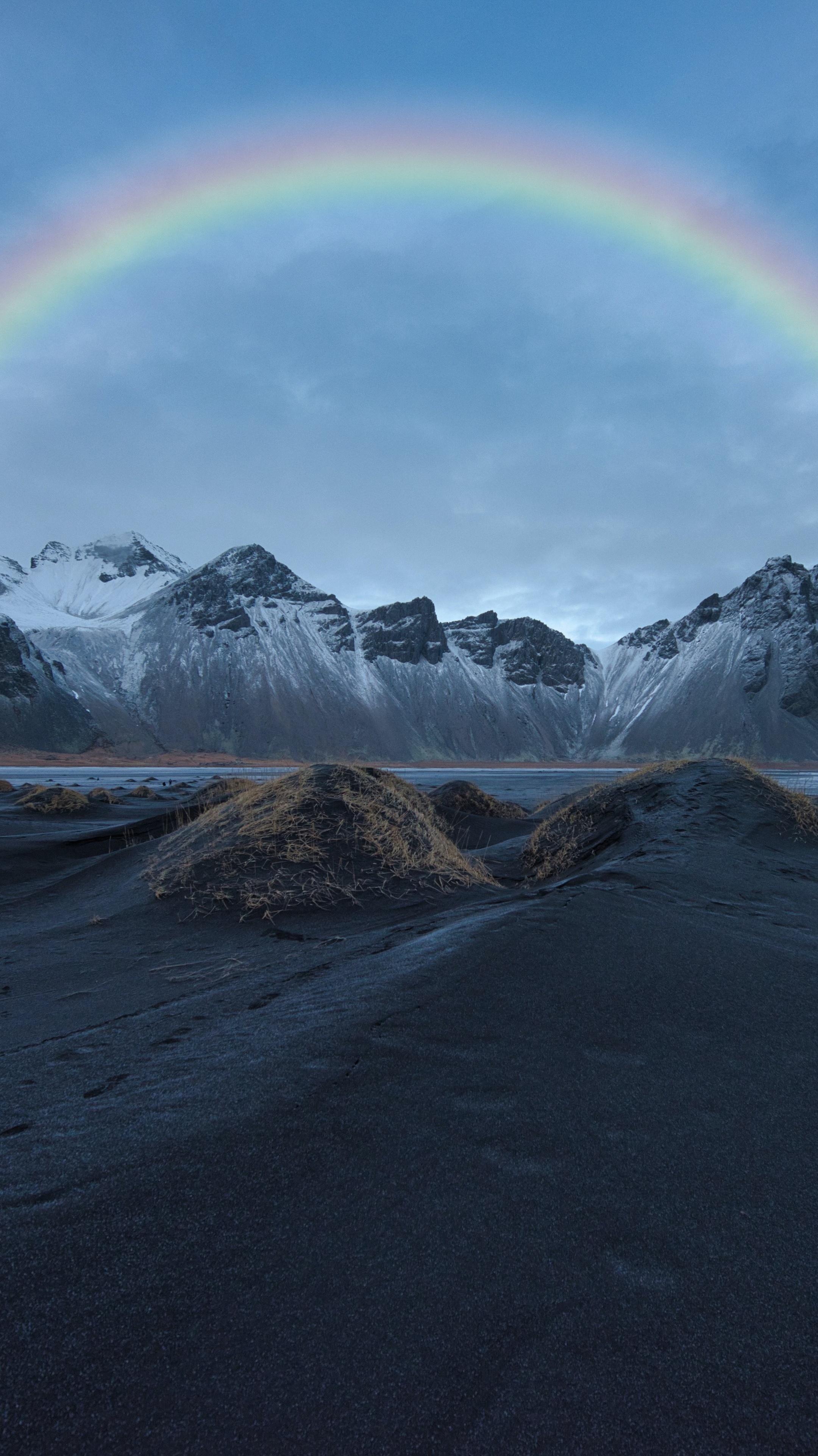 Rainbow over snow-capped mountains and black sand dunes HD Phone Wallpaper