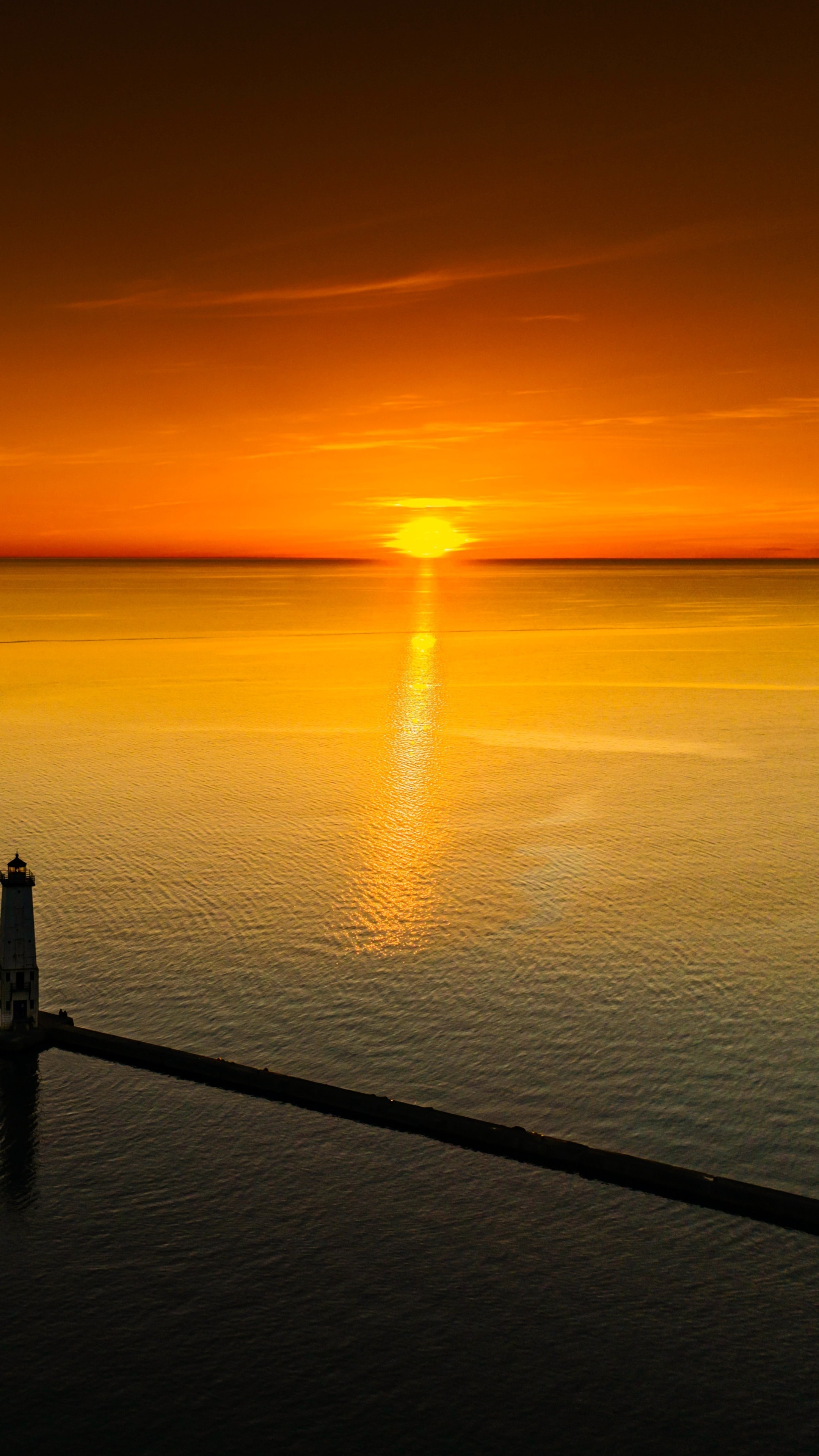 Sunset over the ocean with a lighthouse and pier HD Phone Wallpaper