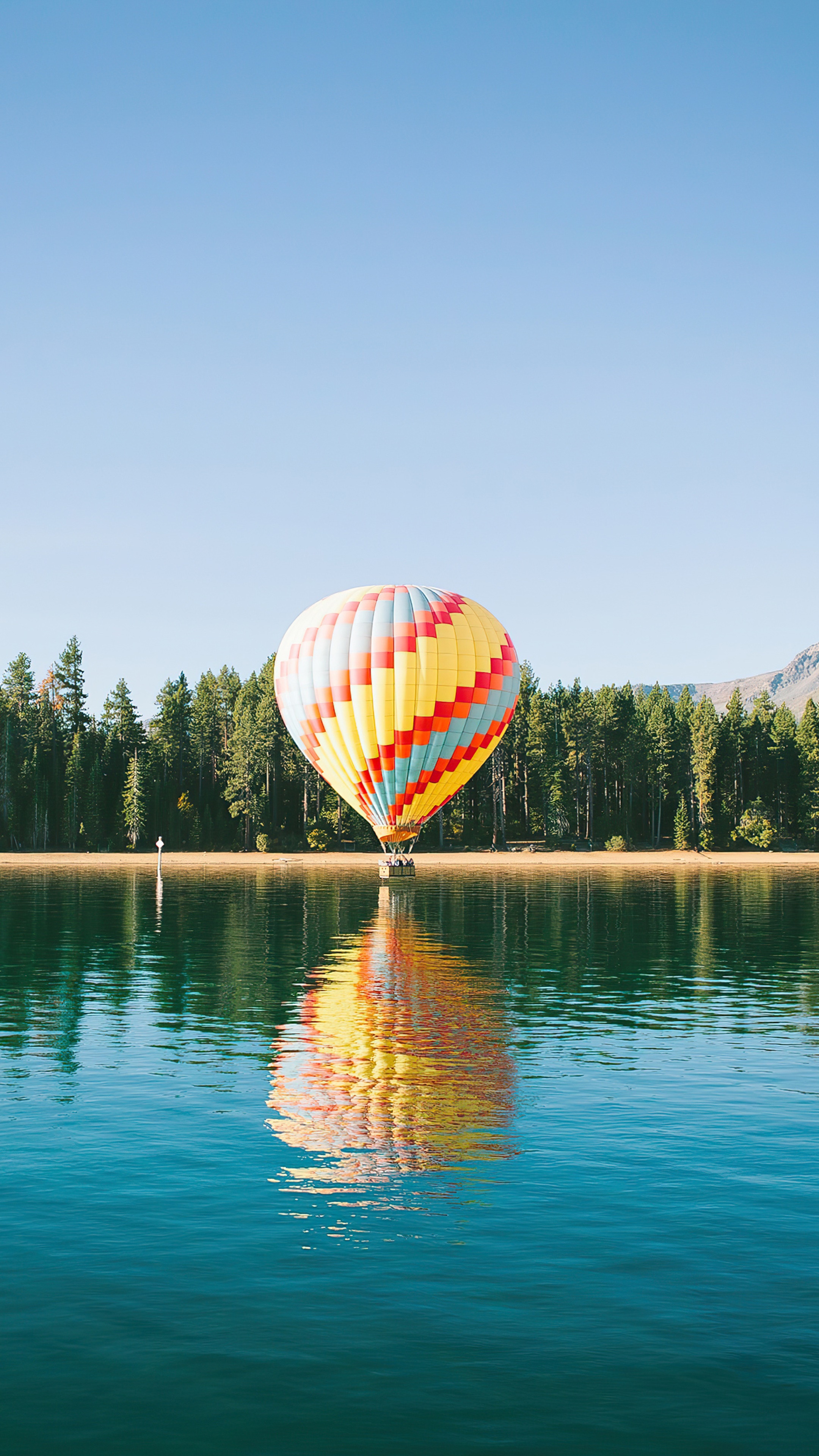 Hot air balloon over a lake with forest background HD Phone Wallpaper