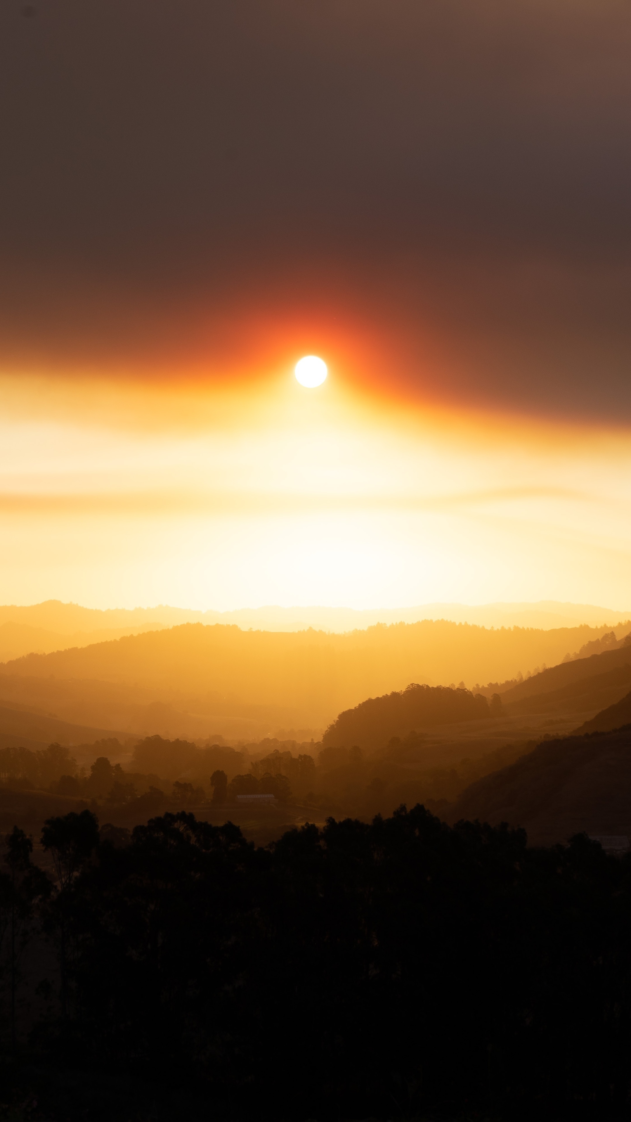 Sun obscured by smoke over rolling hills HD Phone Wallpaper