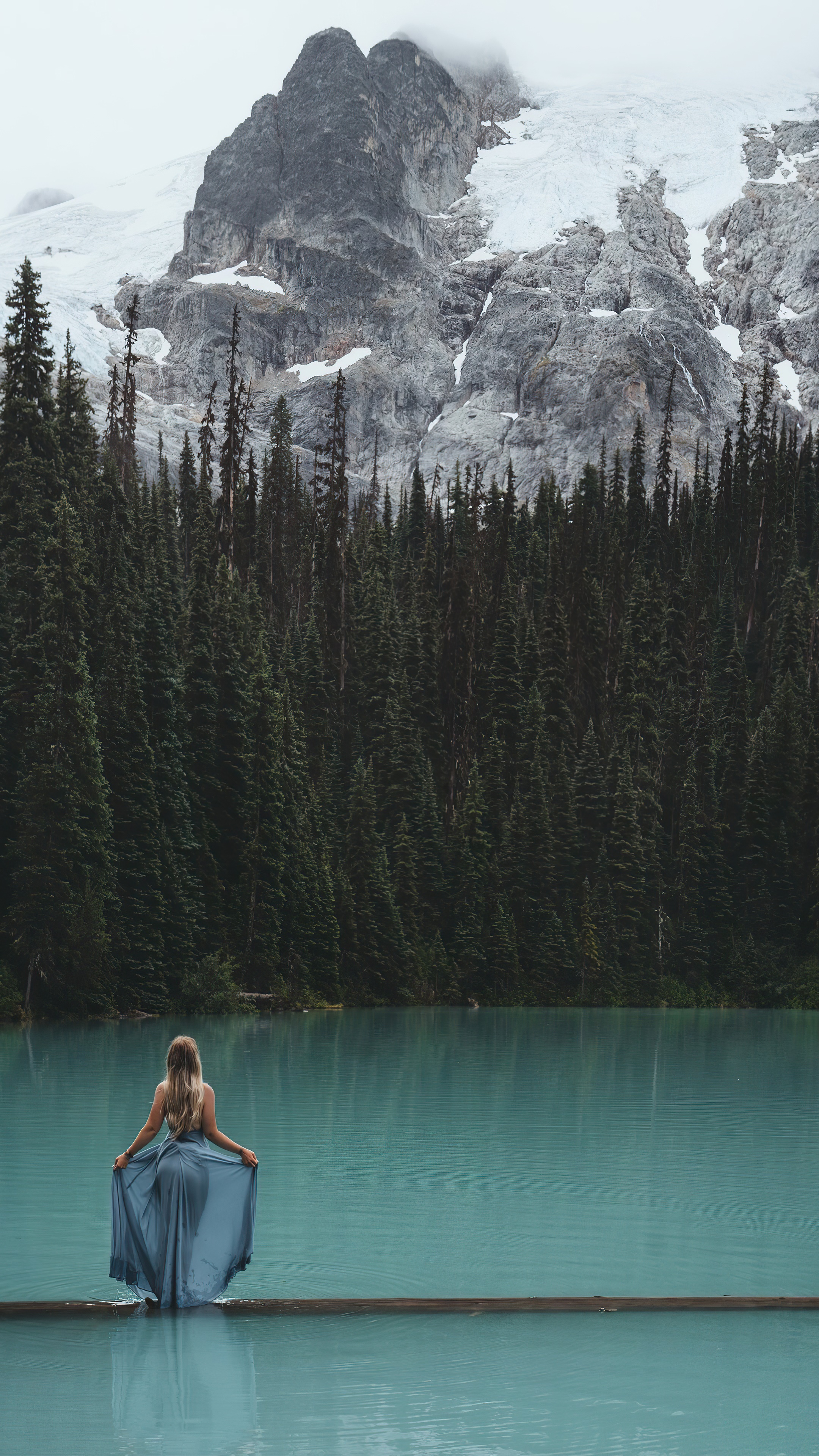 Woman in a blue dress on a log in a lake with mountains HD Phone Wallpaper