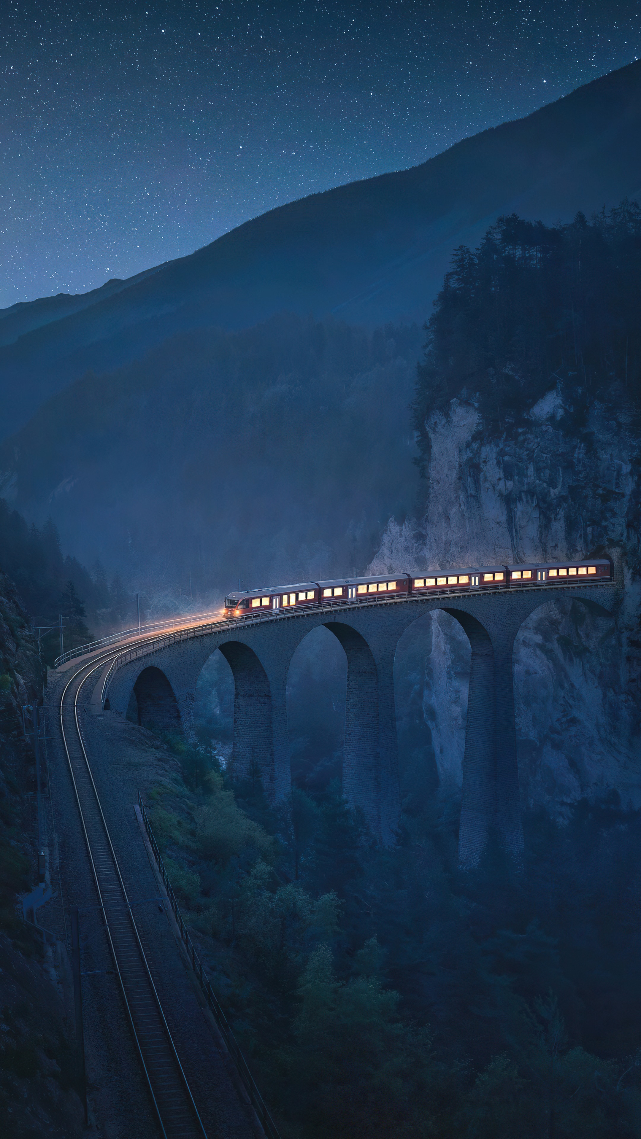 Train crossing a bridge in mountains at night 4K HD Phone Wallpaper