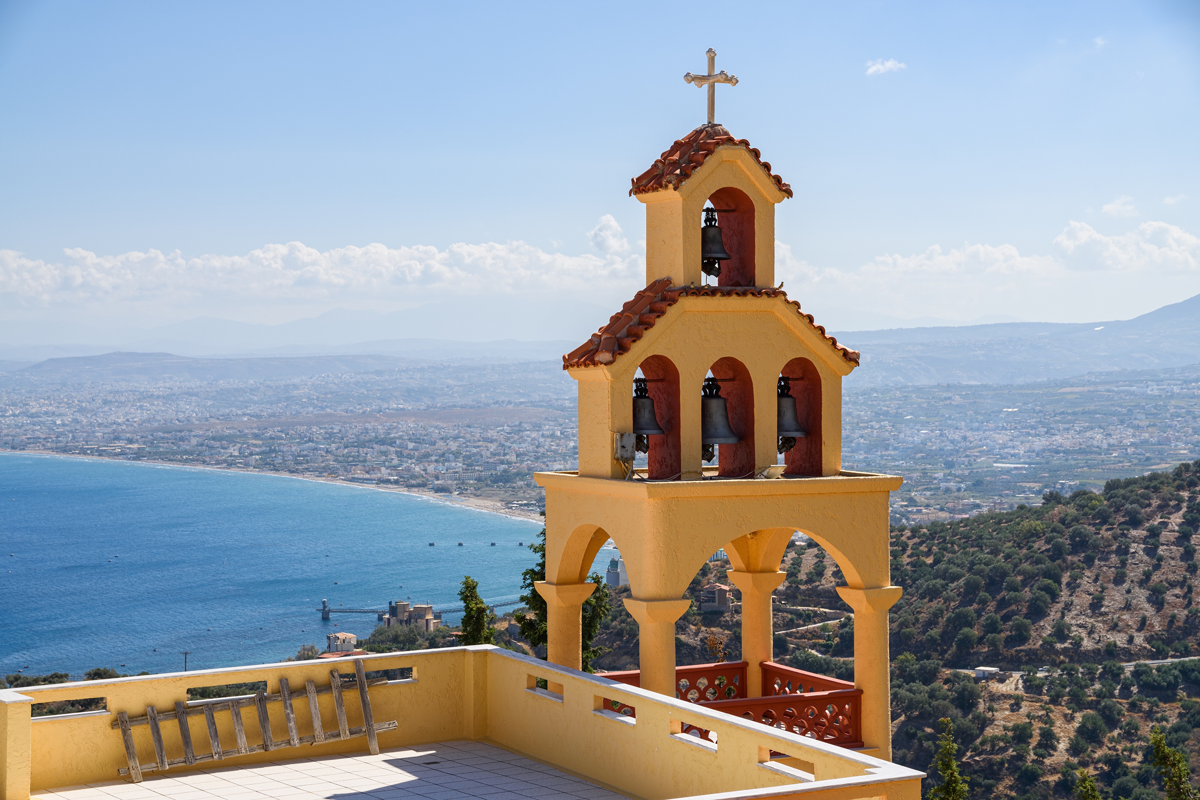 Bell tower with cross overlooking a coastal city in Crete, Greece HD Wallpaper