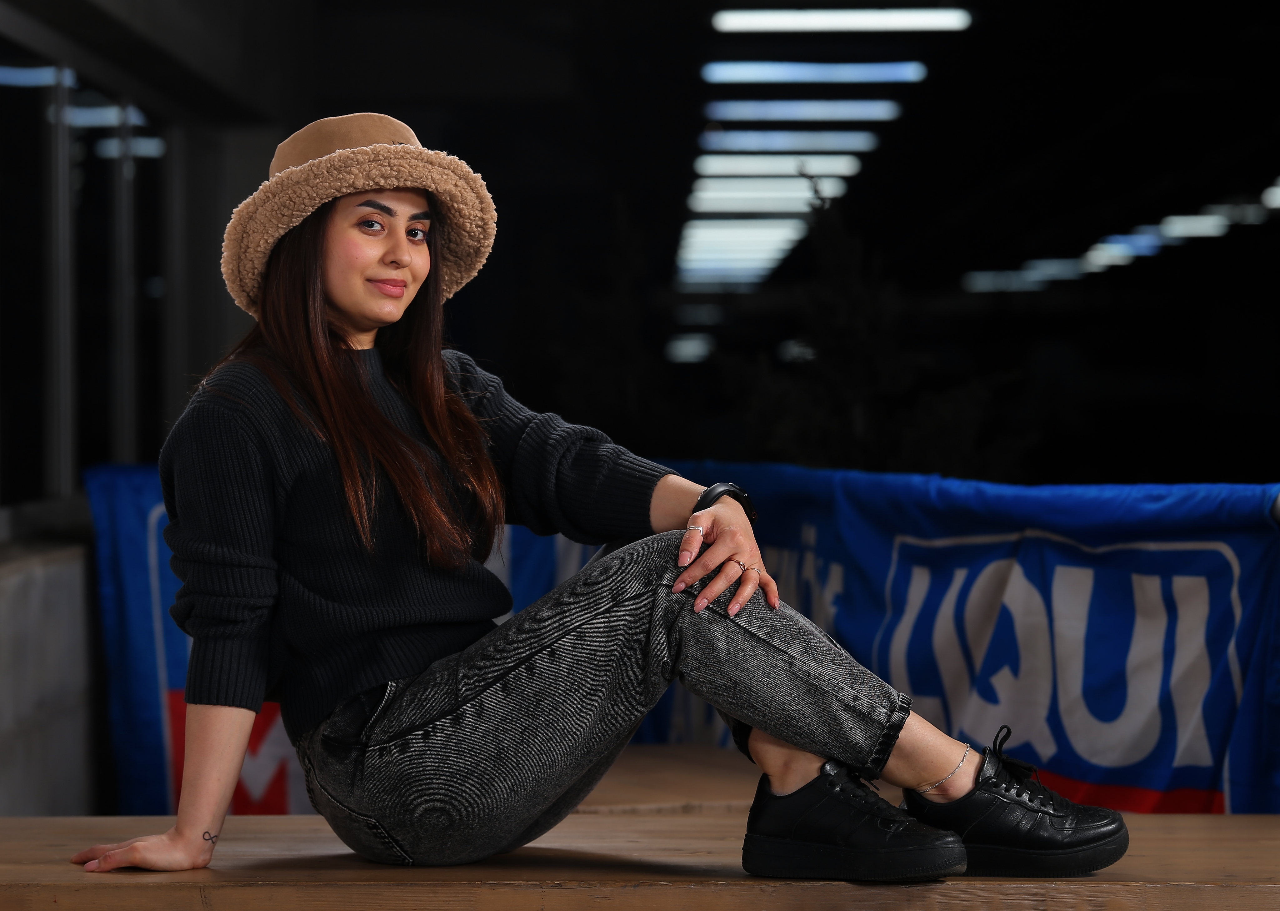 Woman in sweater, jeans, and hat sitting HD Wallpaper