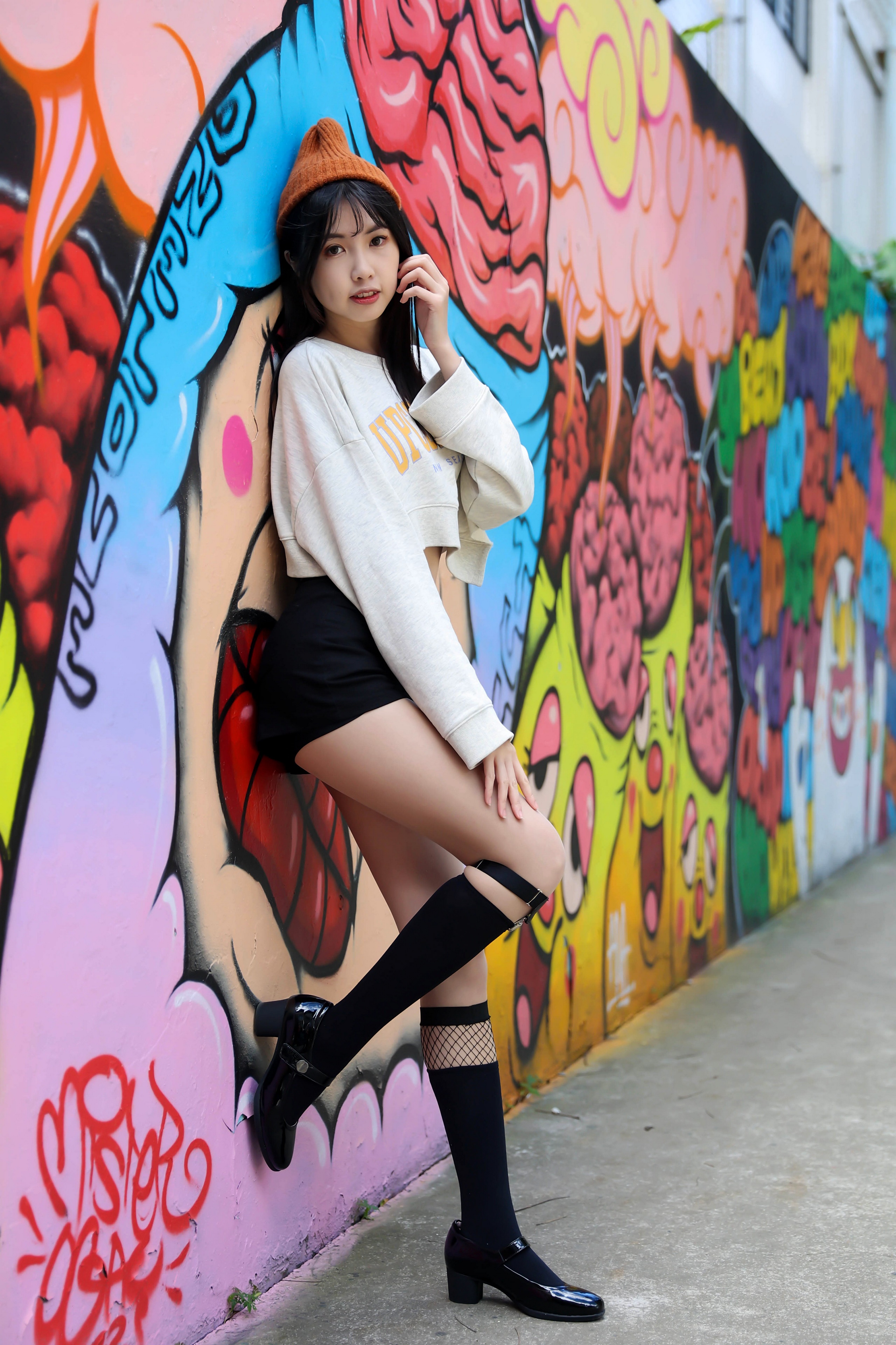 Asian woman in shorts and sweater posing by graffiti wall HD Phone Wallpaper