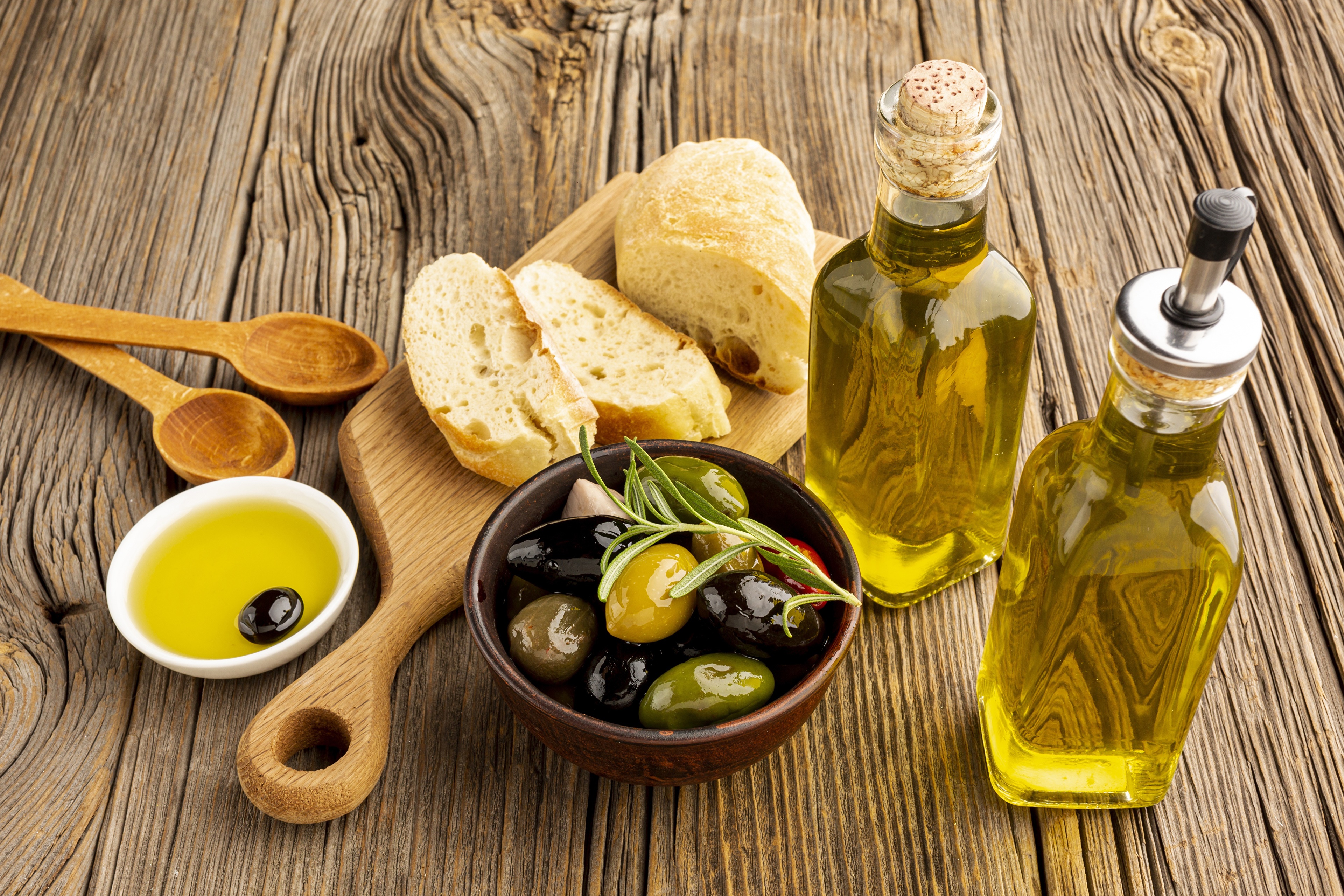Olive oil, olives, bread, and spoons on a wooden table HD Wallpaper