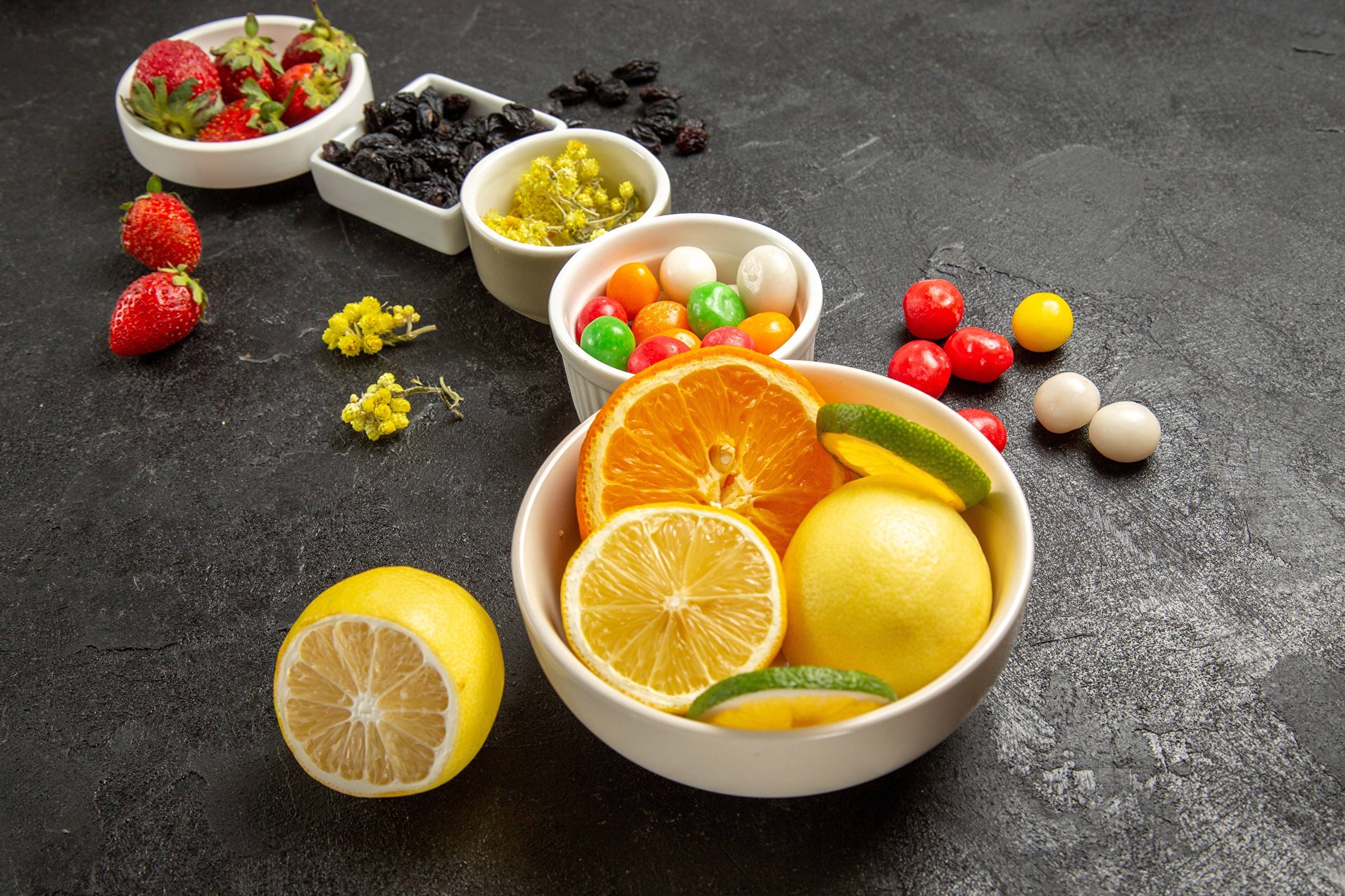 Bowls of fruit, dragees, and strawberries on a dark surface HD Wallpaper