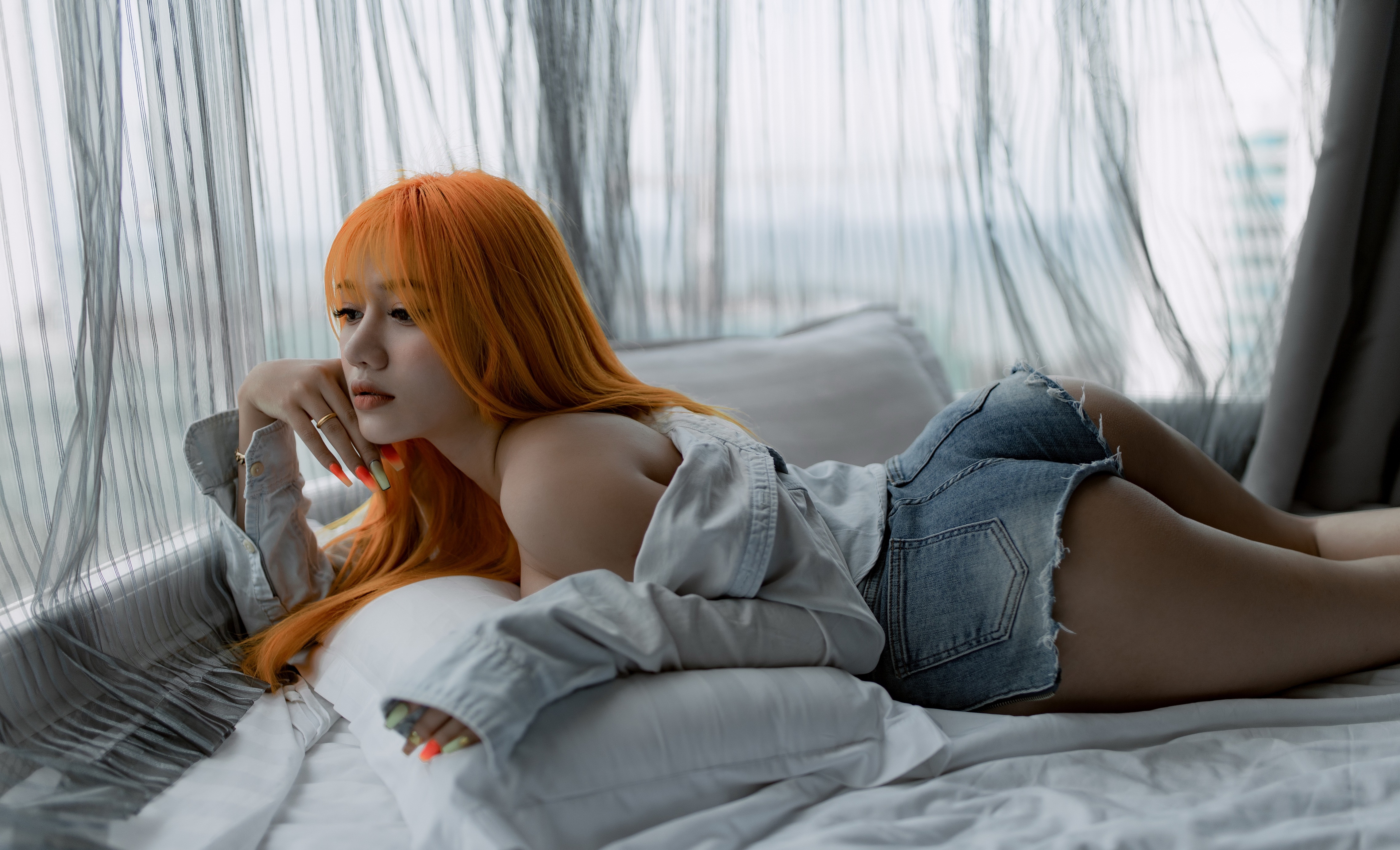 Asian woman with orange hair in denim shorts lying on bed HD Wallpaper