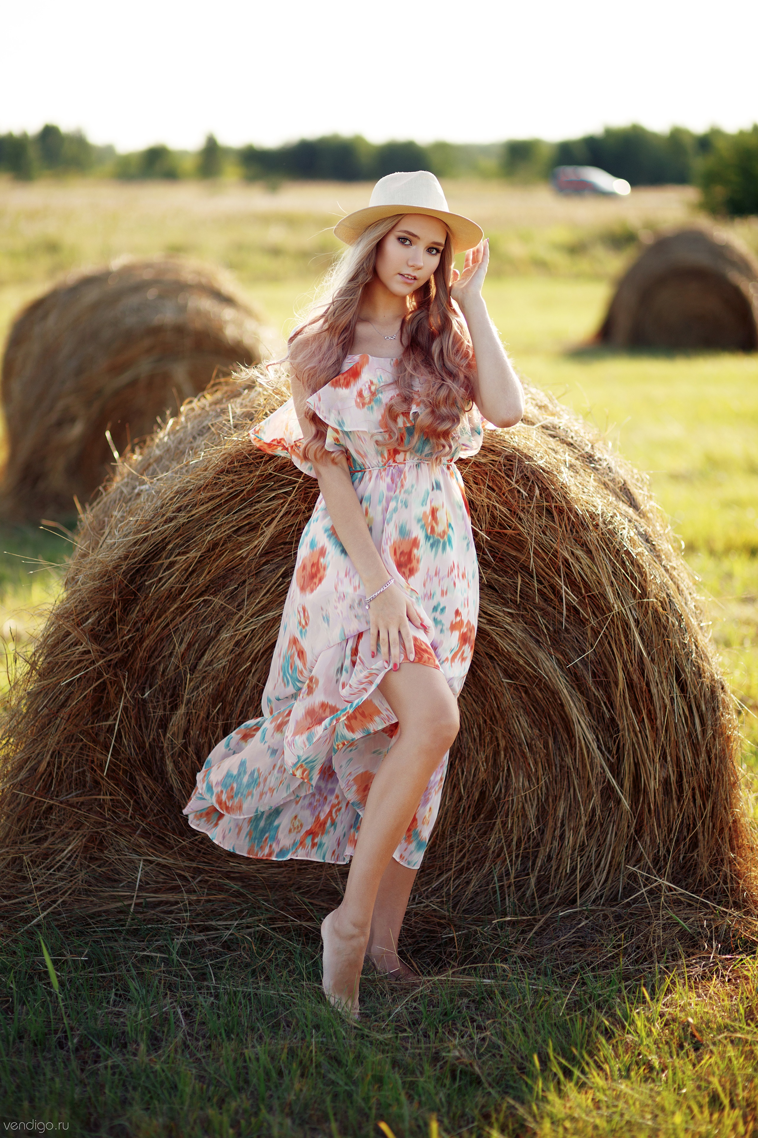 Woman in a floral dress and hat posing by hay bales HD Phone Wallpaper