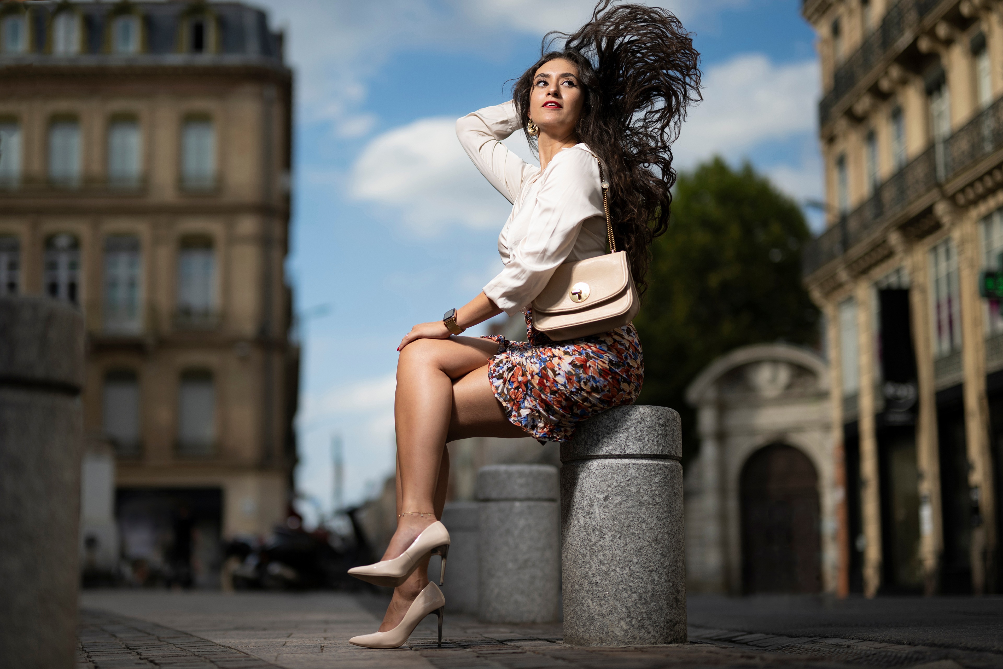 Brunette girl in skirt and stilettos sitting on bollard HD Wallpaper