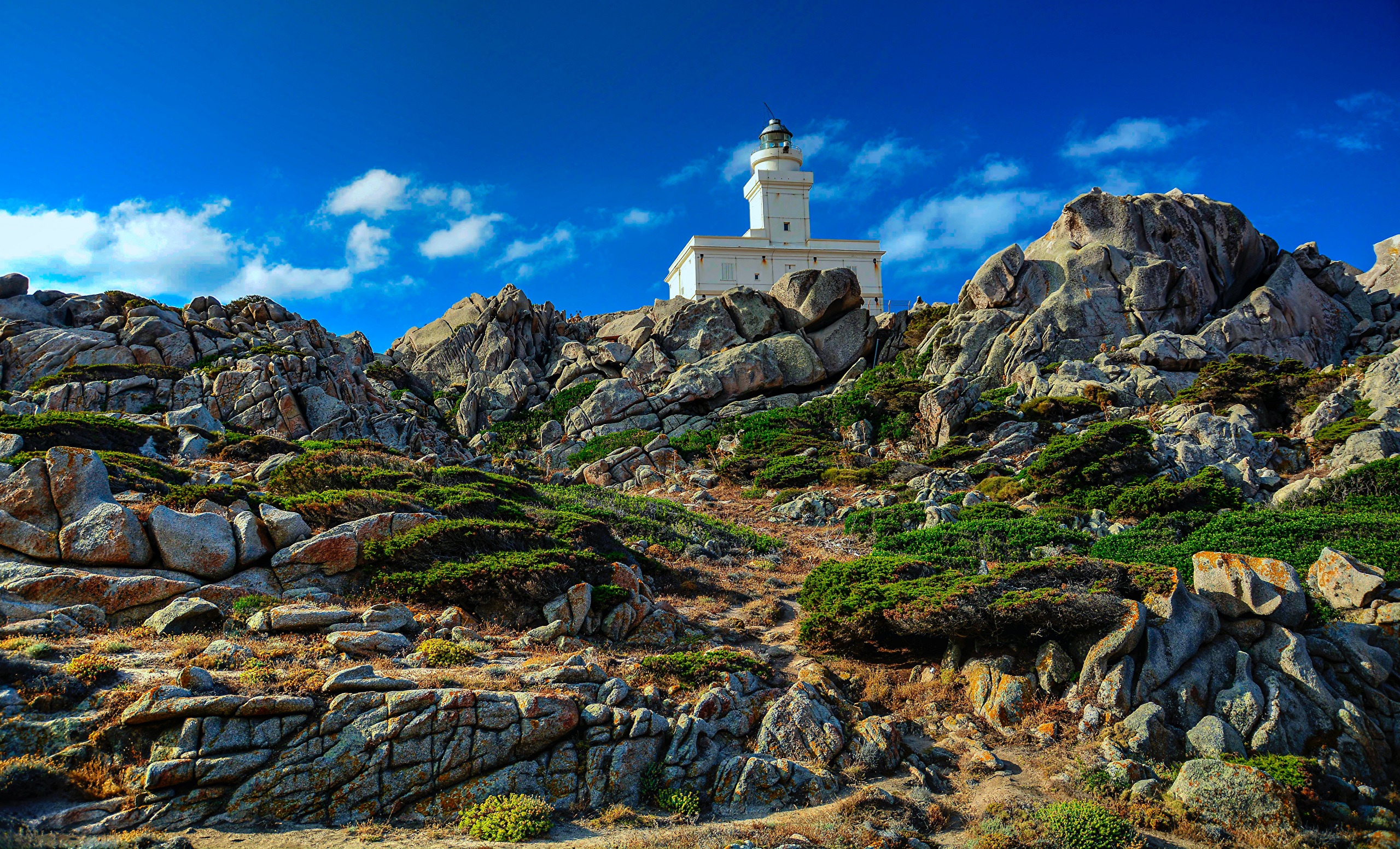 White lighthouse on rocky coast of Capo Testa, Italy HD Wallpaper