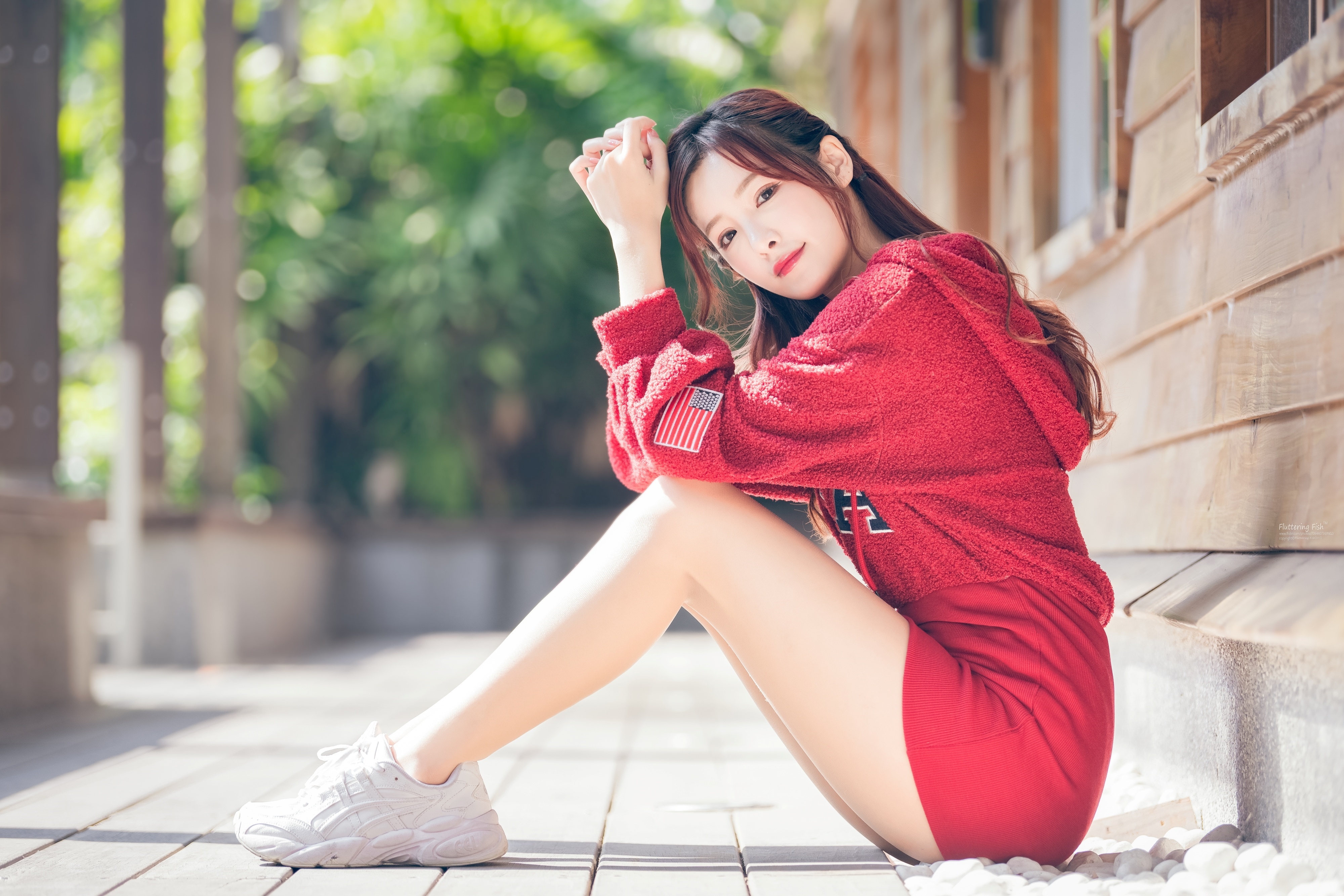 Brunette girl in red hoodie sitting outdoors HD Wallpaper