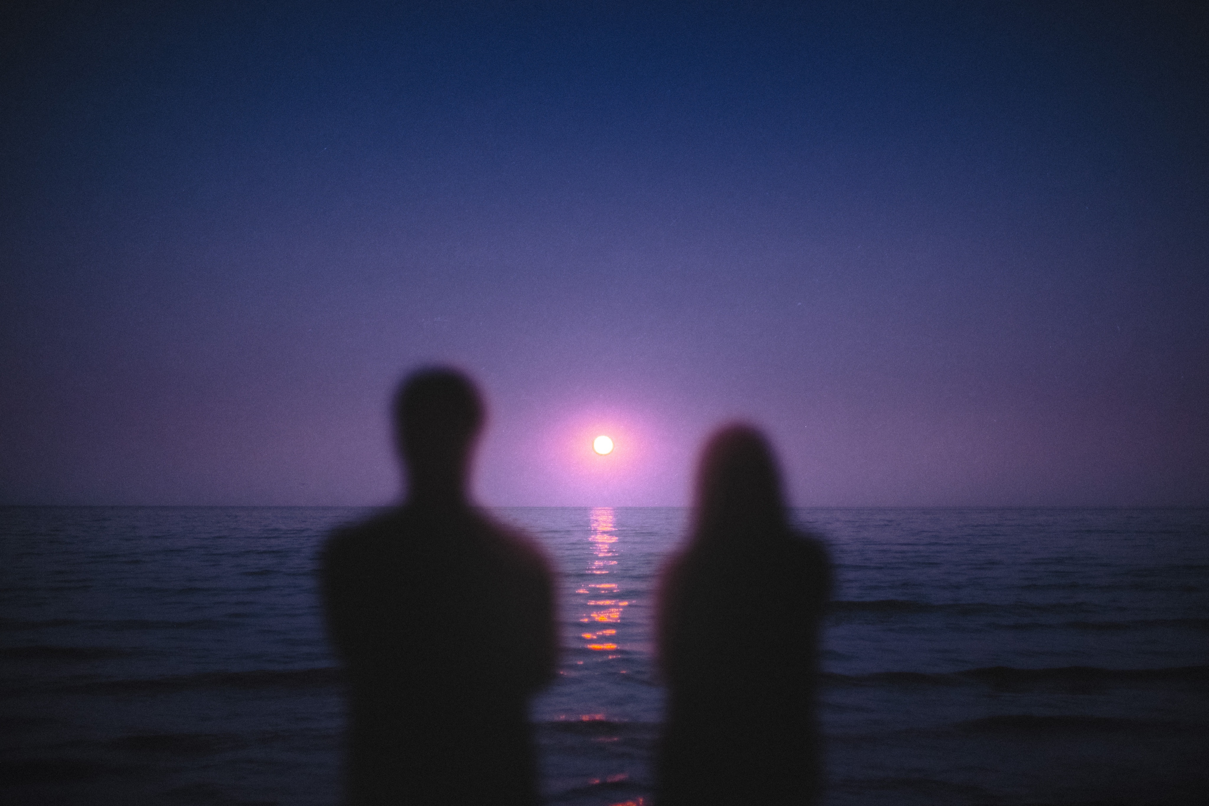 Couple watching the sunset over the ocean HD Wallpaper